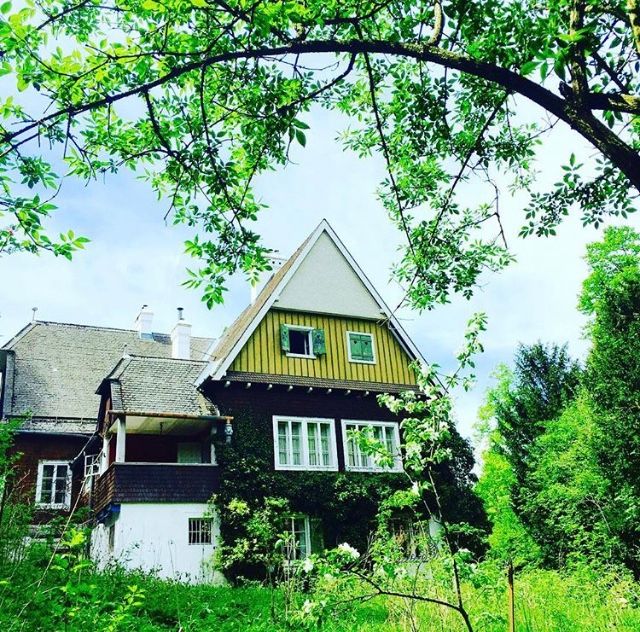 Ein traditionelles Haus mit Satteldach, umgeben von grünen Bäumen und Pflanzen.