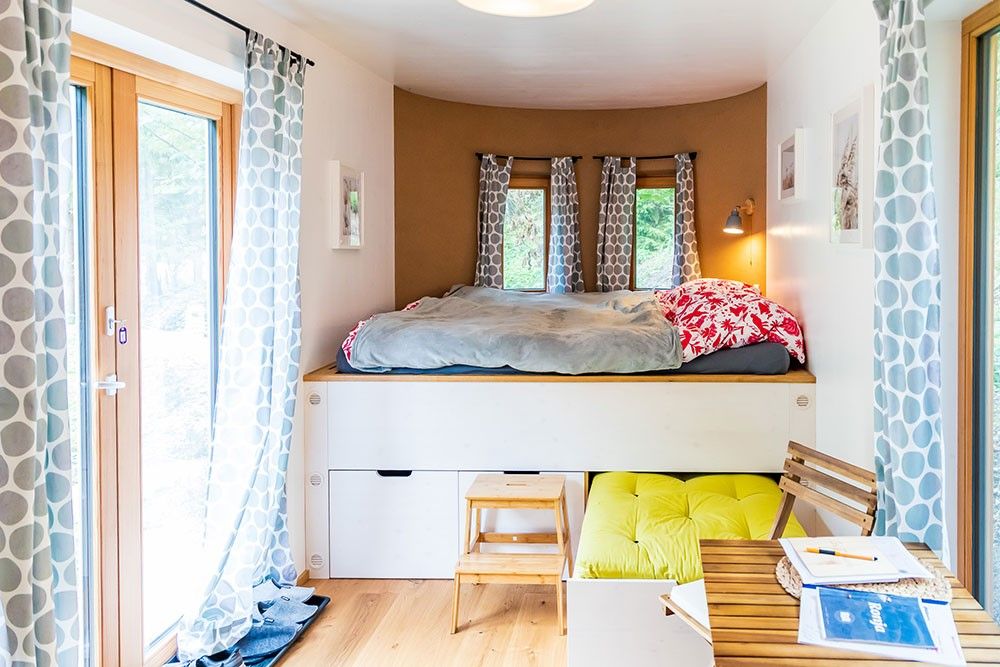 Gemütlicher Schlafbereich mit Hochbett, Vorhängen und kleinem Tisch in einem hellen Raum.