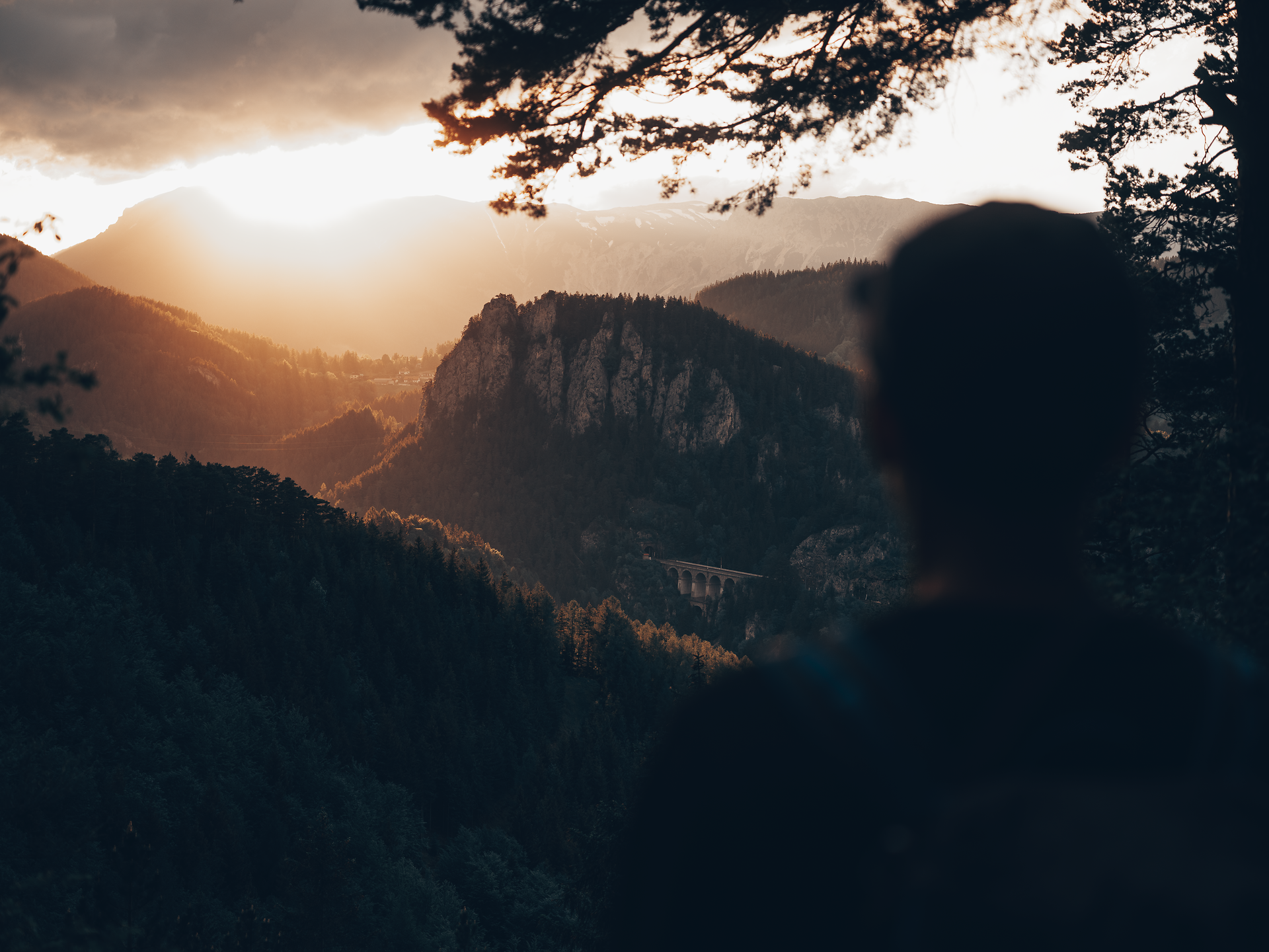 Die sanften Hügel der Wiener Alpen erstrahlen im warmen Licht der untergehenden Sonne. Ein Wanderer genießt den atemberaubenden Ausblick auf die majestätischen Berge und die üppige, grüne Landschaft, die sich bis zum Horizont erstreckt. Diese friedliche Szenerie lädt dazu ein, die Schönheit der Natur in vollen Zügen zu erleben.