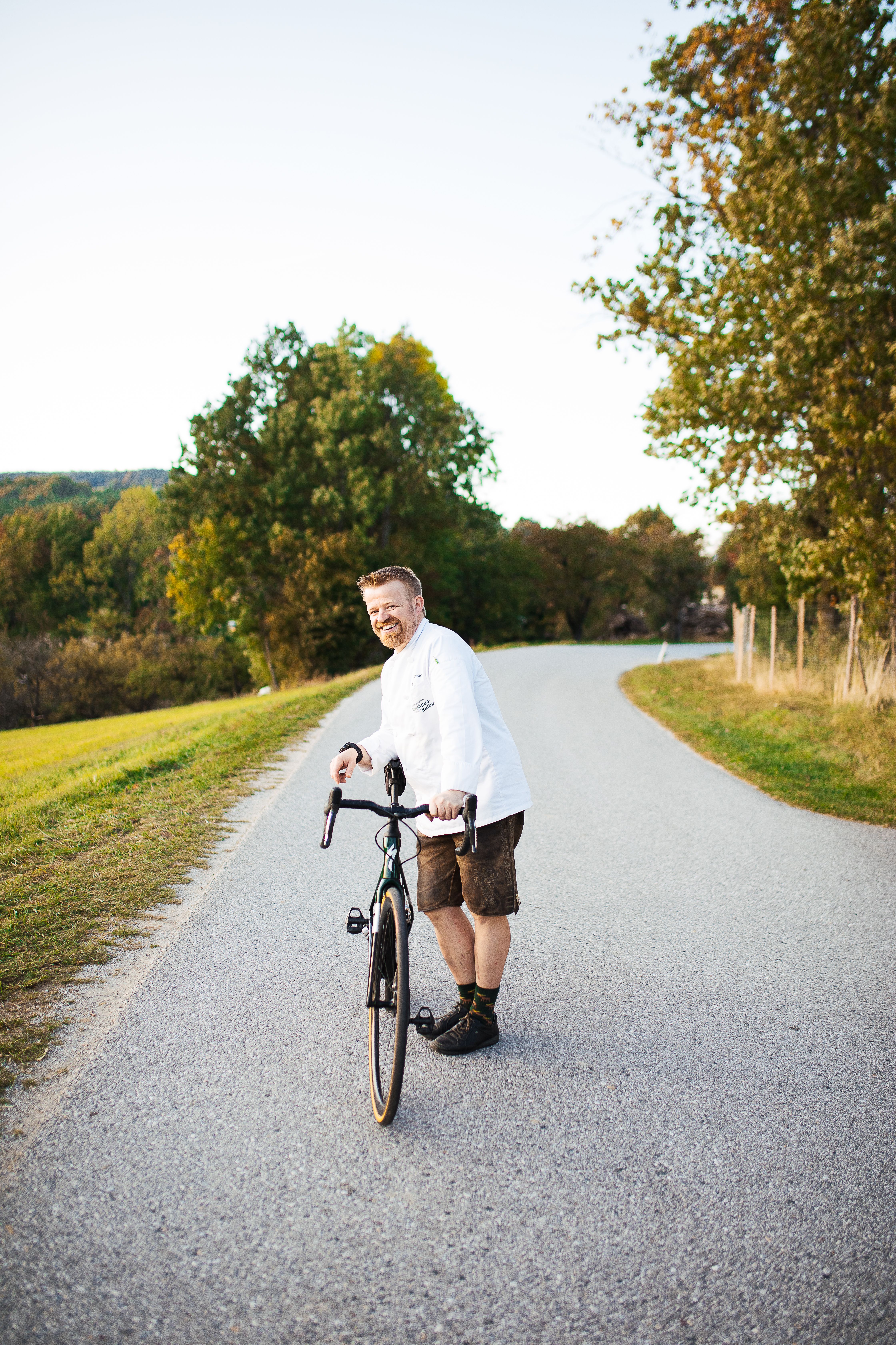 Ein strahlender Tag in den Wiener Alpen lädt zu einer erfrischenden Radtour ein. Der Wirt Andreas Ottner genießt die malerische Landschaft und die frische Luft, während er sein Rad schiebt. Umgeben von üppigem Grün und sanften Hügeln ist dies der perfekte Ort, um die Seele baumeln zu lassen.