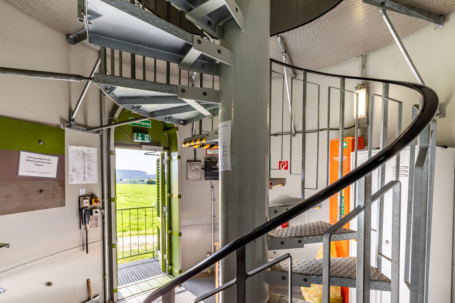 Innenansicht eines Windrads mit Wendeltreppe und geöffneter Tür nach draußen.