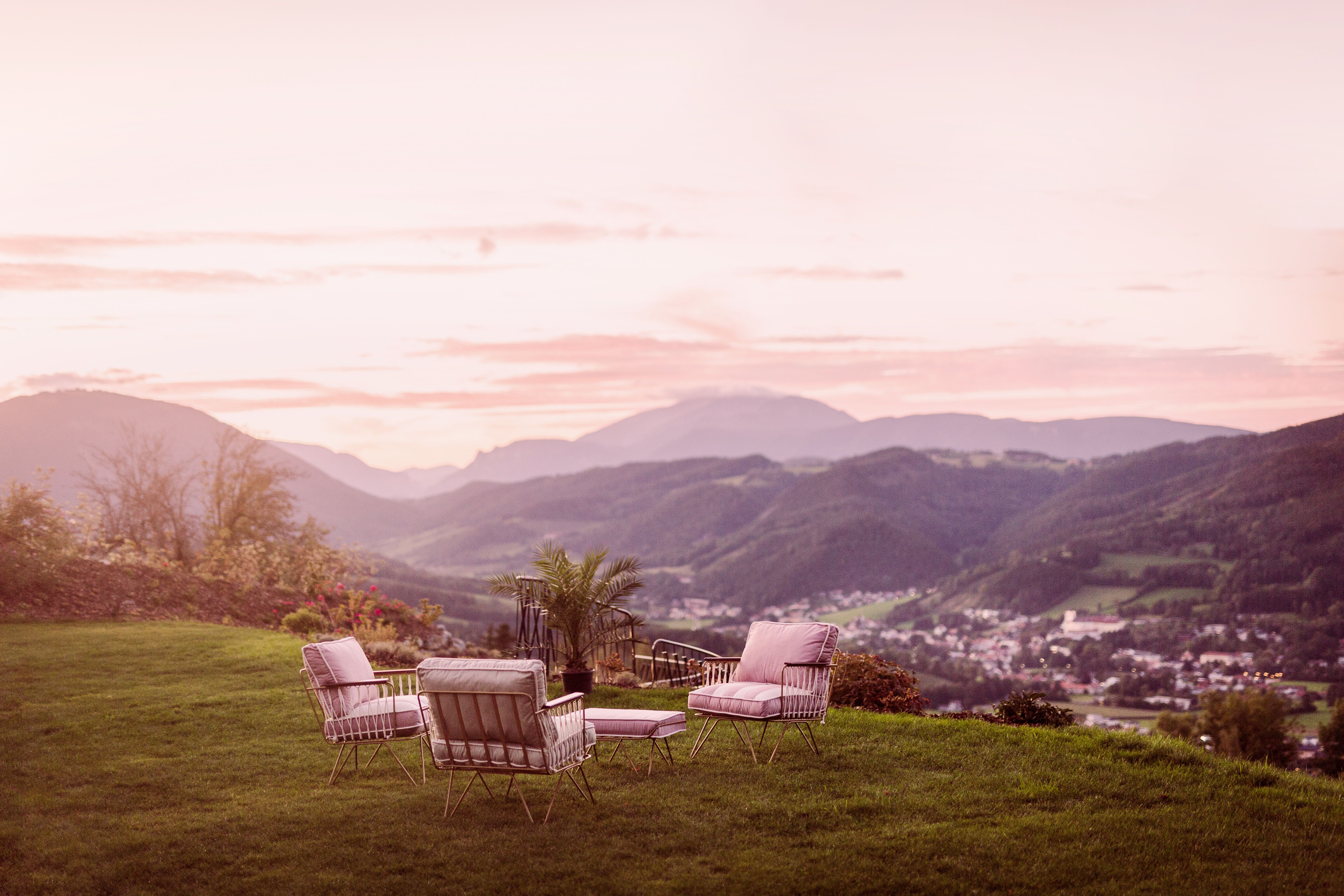 Gartenmöbel auf einer Wiese mit Blick auf eine Berglandschaft bei Sonnenuntergang.
