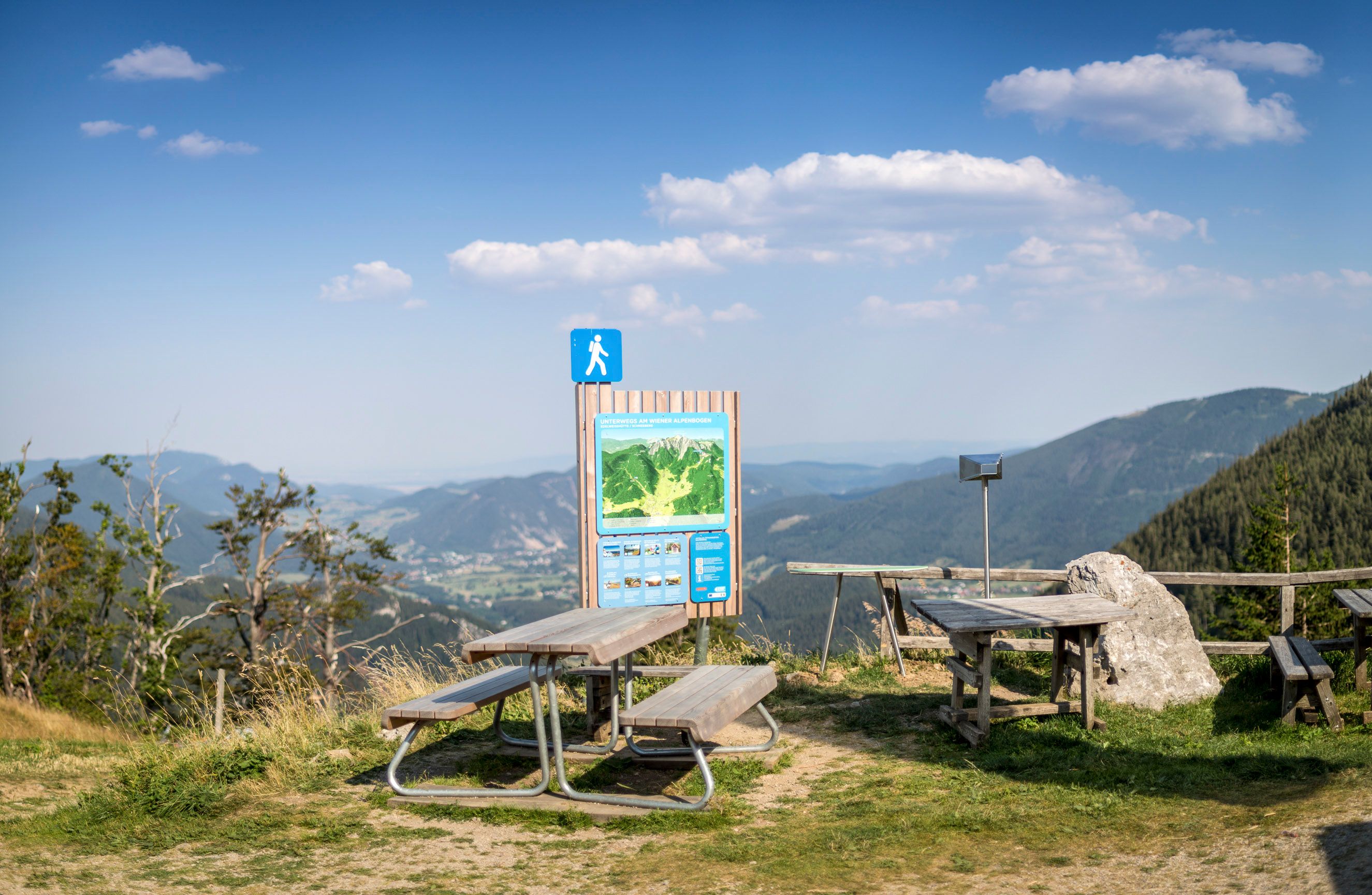 Picknicktische und Wanderschild mit Bergblick bei der Edelweißhütte am Schneeberg.