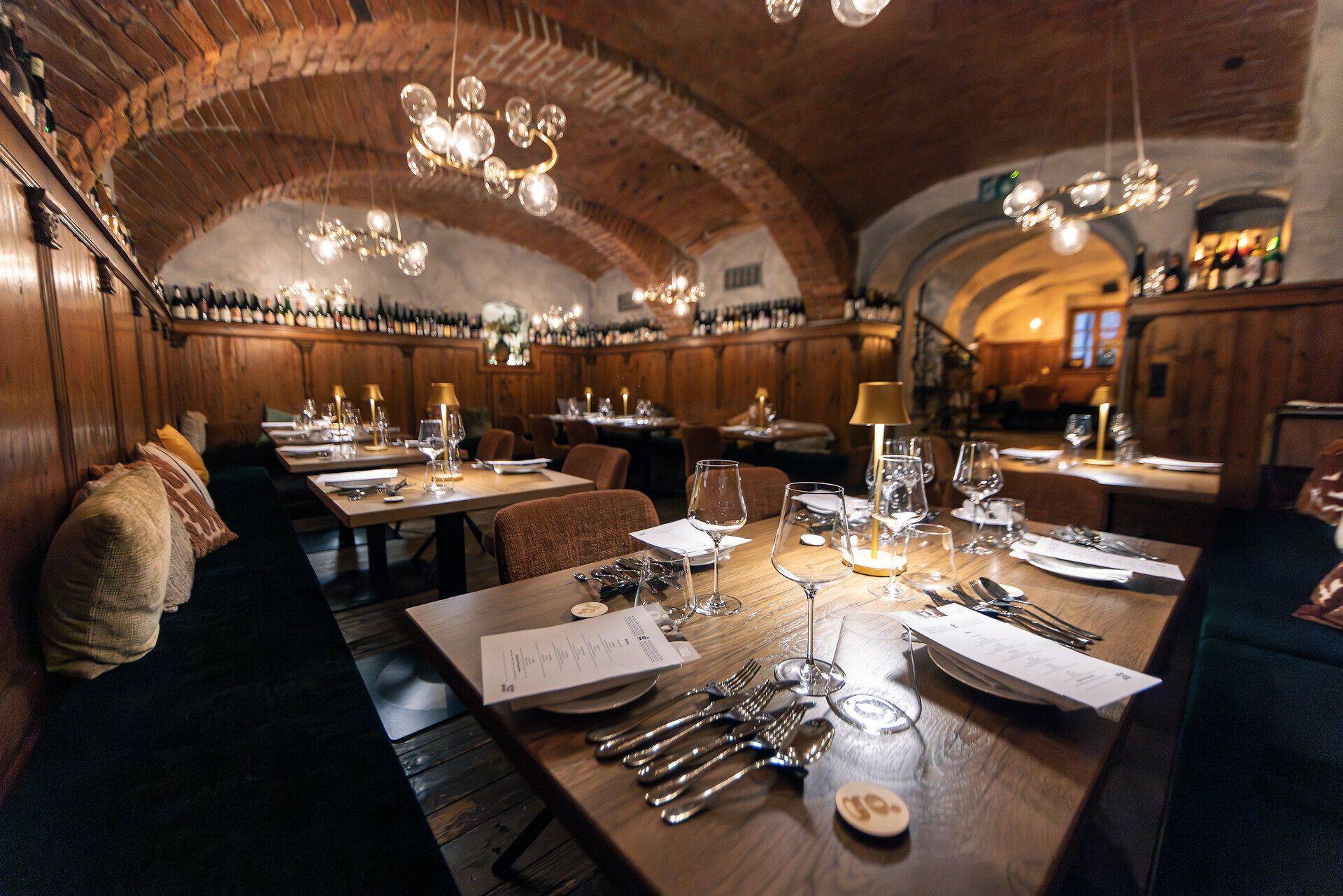 In einer rustikalen, edlen Gaststube mit Gewölbe sind viele Tische fein gedeckt. 