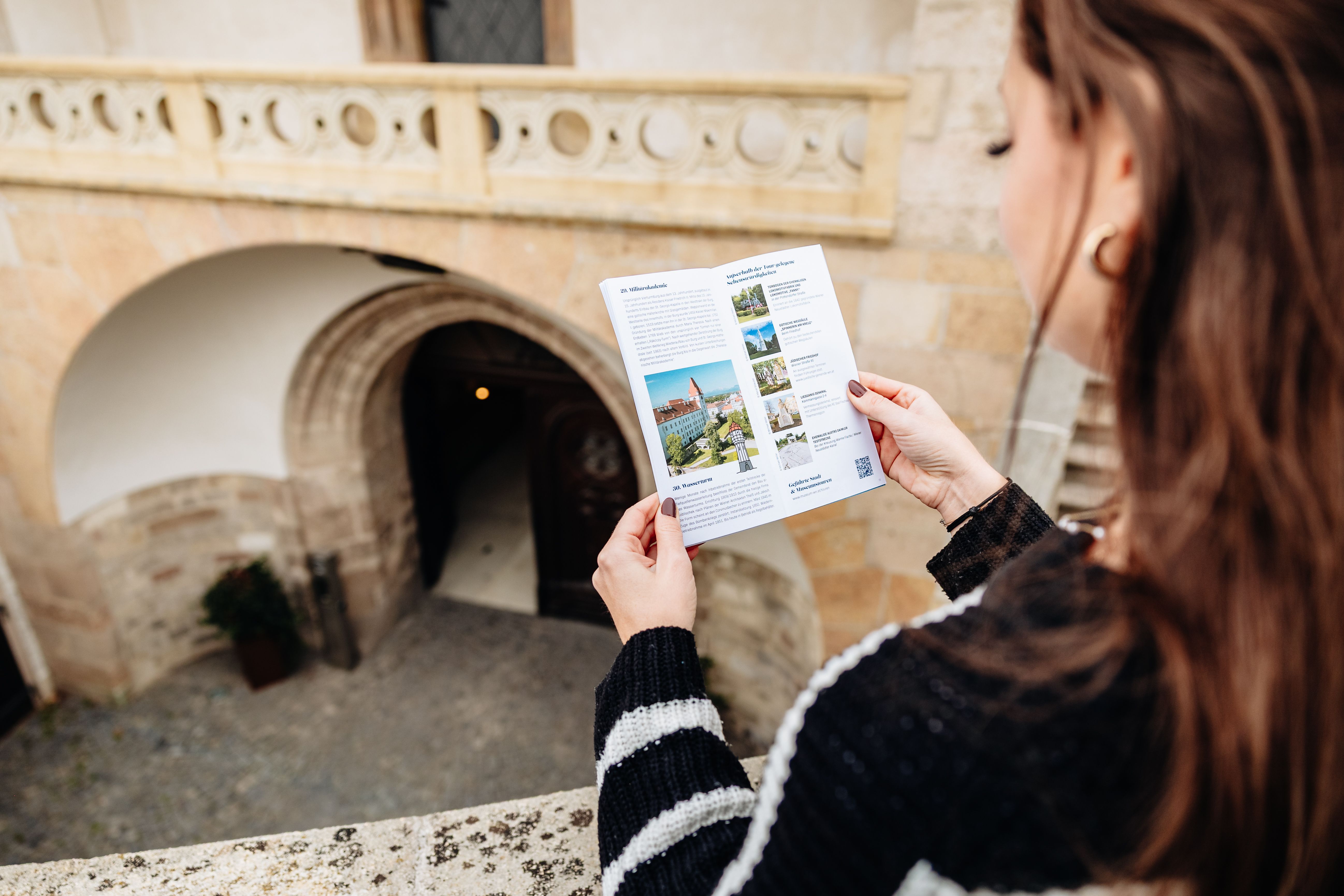 Frau steht mit einem Flyer auf einem Balkon. 
