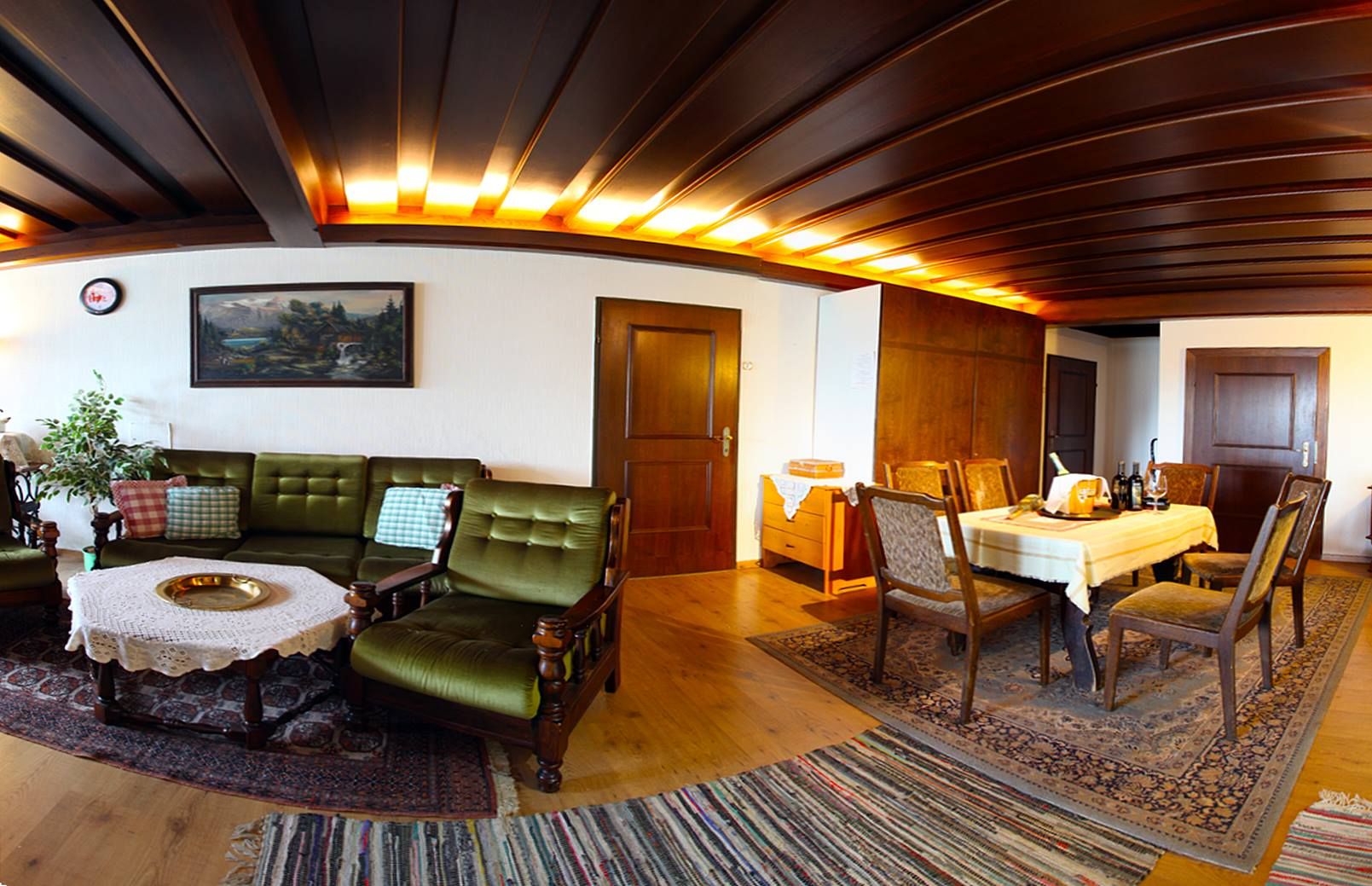 Gemütliches Wohnzimmer mit Holzmöbeln, grünem Sofa, Esstisch und Teppichen.