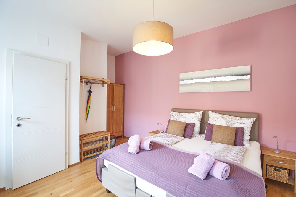 Ein gemütliches Gästezimmer mit rosa Wand, Doppelbett und moderner Einrichtung.