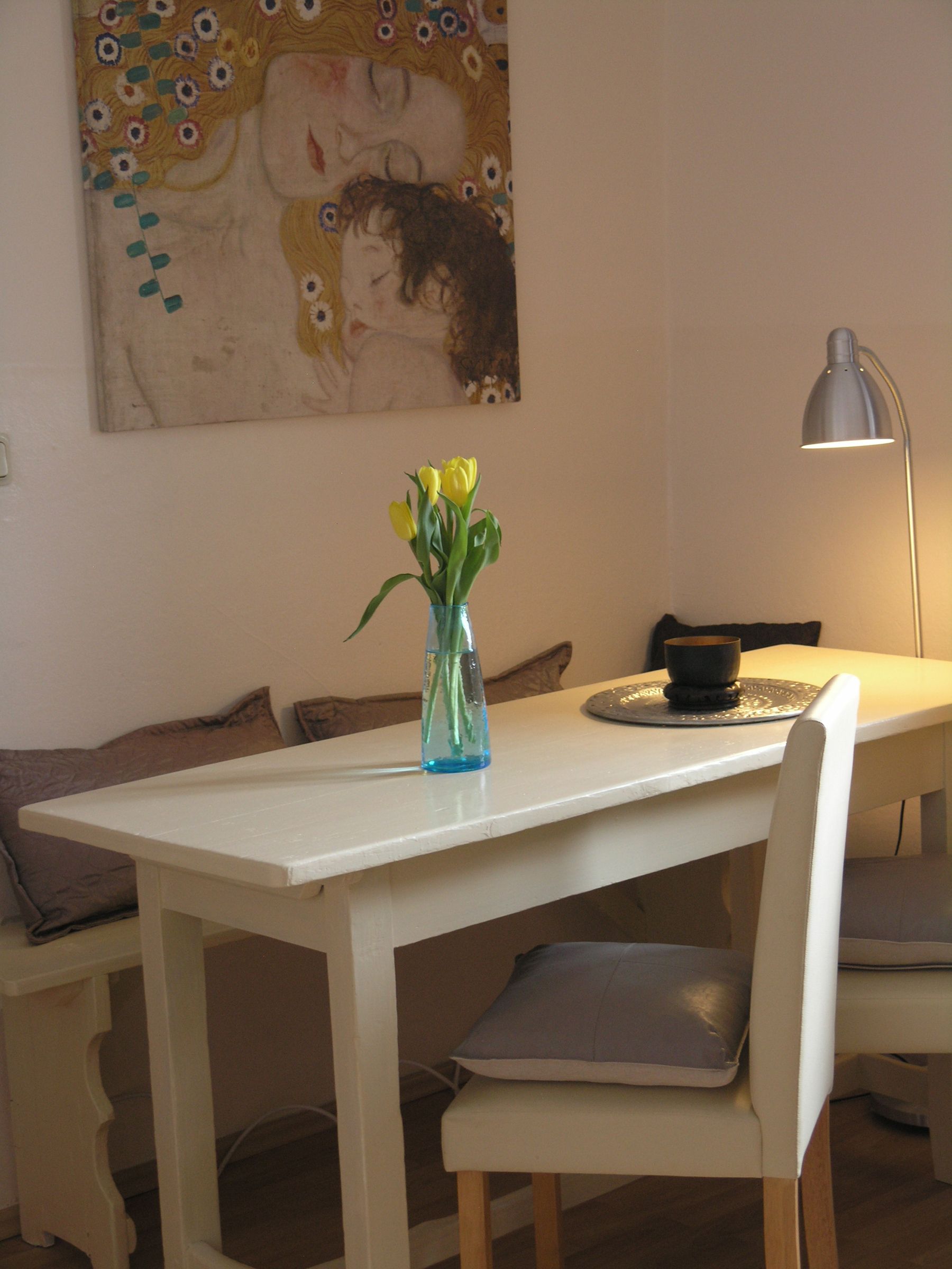 Ein gemütlicher Essbereich mit einem weißen Tisch, gelben Tulpen in einer Vase und einem Gemälde an der Wand.