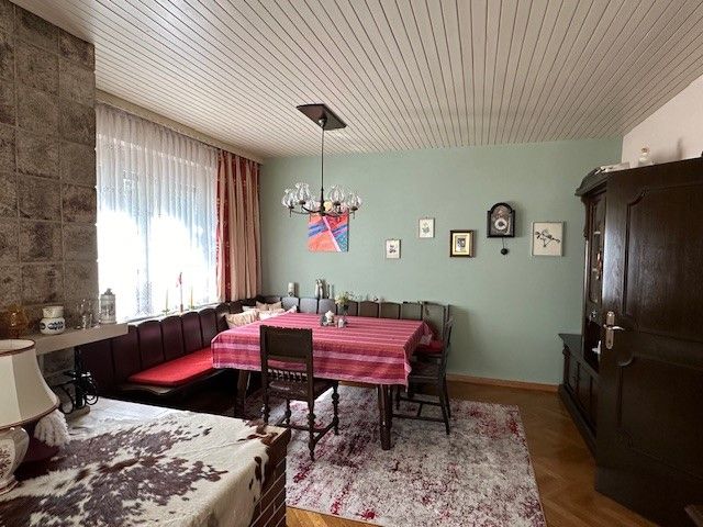 Gemütliches Wohnzimmer mit Esstisch, Eckbank, Teppich und Wanduhr.