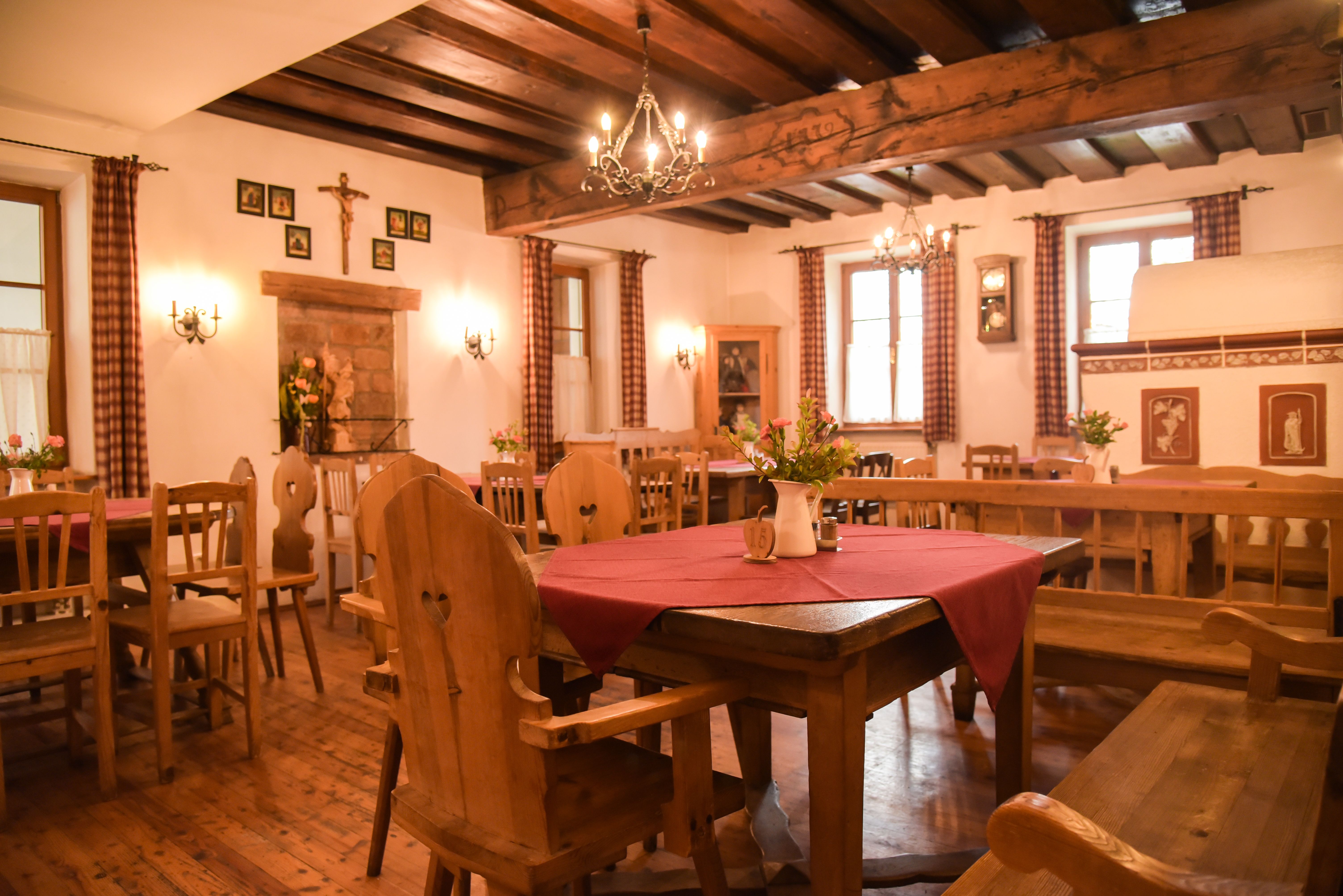 emütliche Stube mit Holzmöbeln, roten Tischdecken und Kronleuchtern.