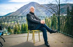 Mann im dunklen Sakko sitzt auf einer Terrasse mit Blick auf Berge und Tallandschaft.