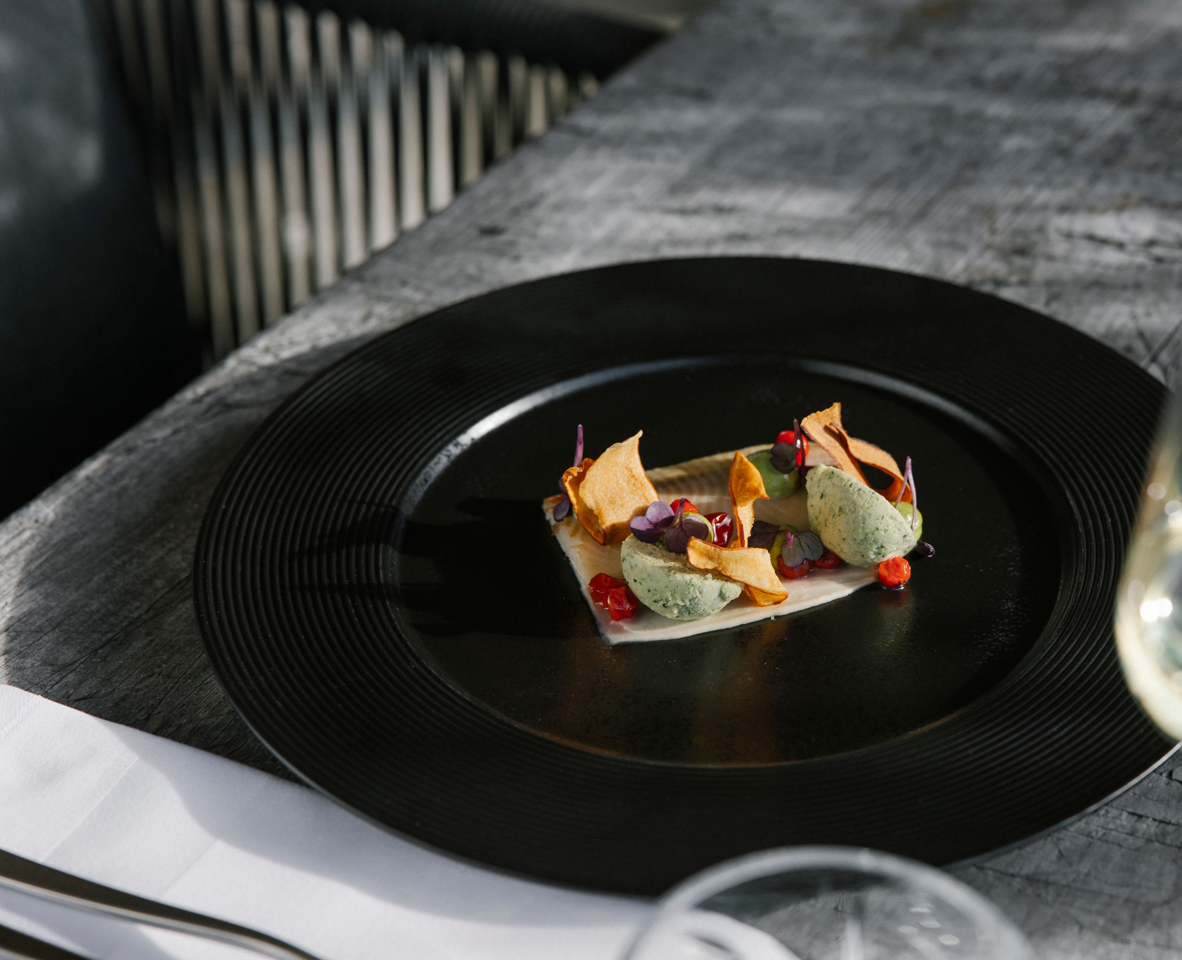 Ein schwarzes Teller mit einer schon angerichteten Vorspeise mit Kräuterbutter, Süßkartoffelstreifen und essbaren Blüten.