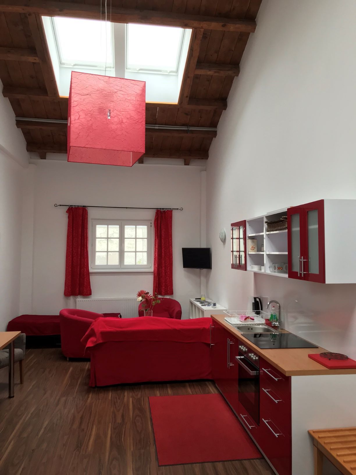 Wohn- und Essbereich in einem Loft mit roten Möbeln und Holzbalkendecke.