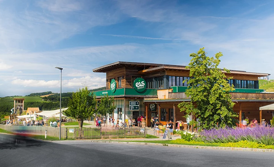 Gebäude der Eis-Greissler Welt mit Bäumen und Besuchern und Blick auf den Erlebnispark.