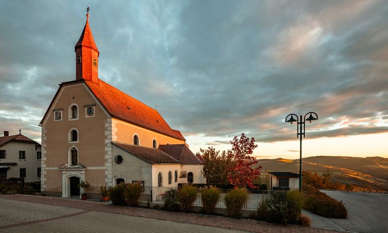 Wallfahrtskirche St. Corona am Wechsel bei Sonnenuntergang mit dramatischem Himmel.