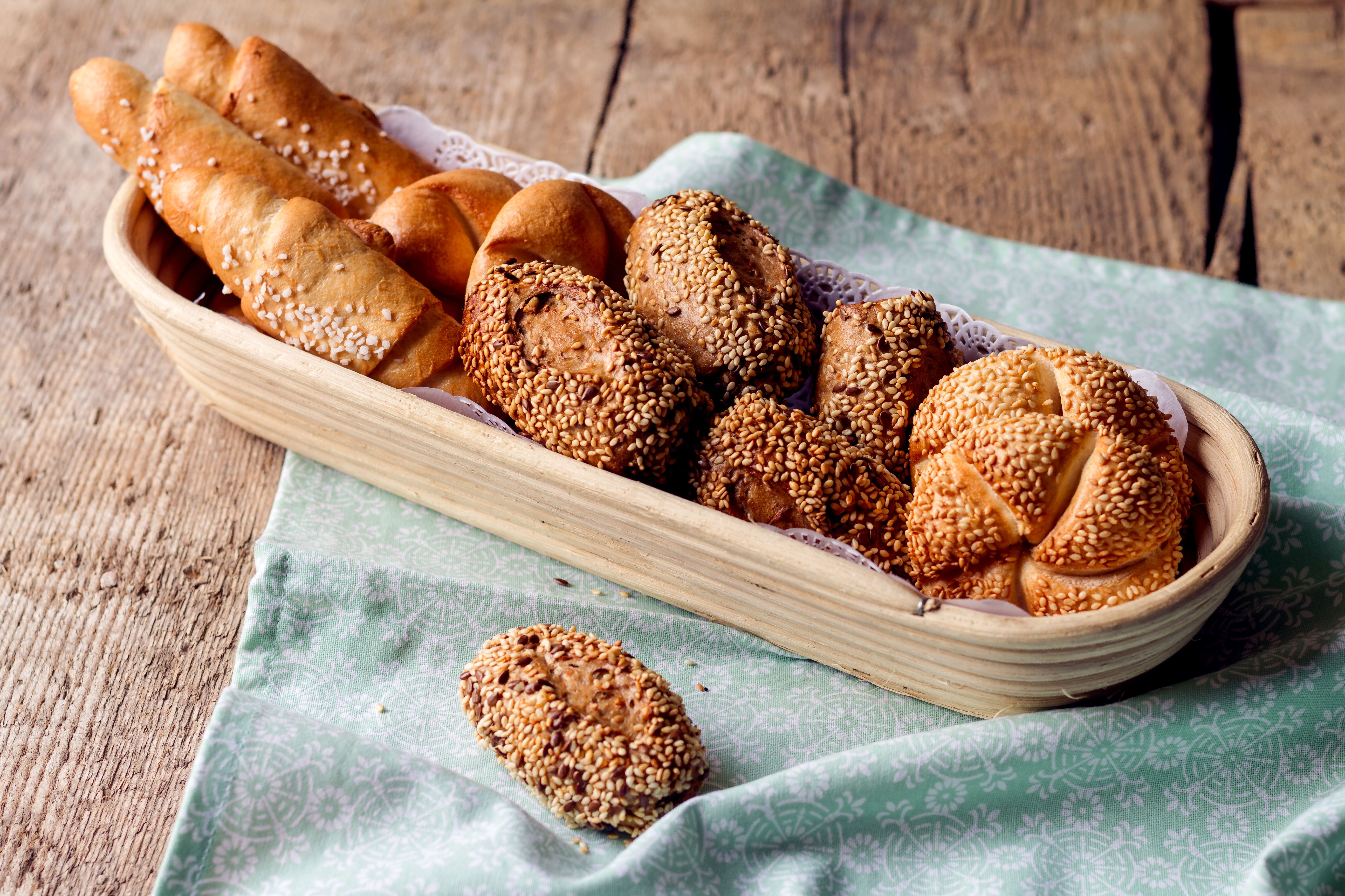 Länglicher Gärkorb mit frischen Gebäck wie Salzstangerl und Semmeln auf einem grünen Tuch mit Mustern.