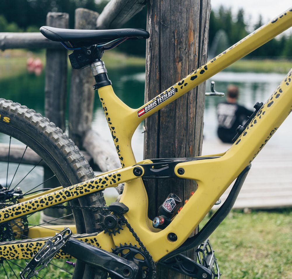 Ein strahlend gelbes Mountainbike mit einem einzigartigen Leopardenmuster steht bereit, um die aufregenden Trails zu erkunden. Im Hintergrund spiegelt sich die ruhige Wasseroberfläche eines Sees, während ein Besucher die friedliche Atmosphäre genießt. Hier in den Wiener Alpen erwartet Abenteurer eine perfekte Kombination aus Natur und Nervenkitzel.