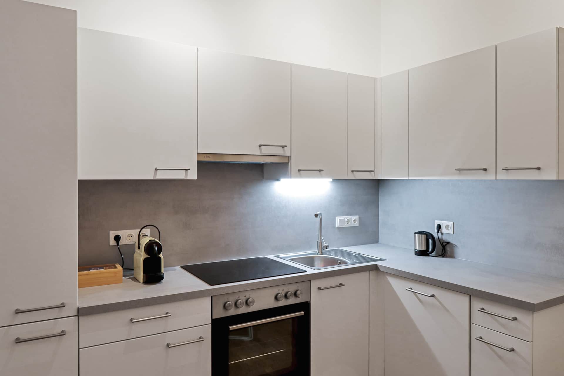 Weiße Küche mit Waschbecken, Herd, Backofen und Kaffeemaschine.