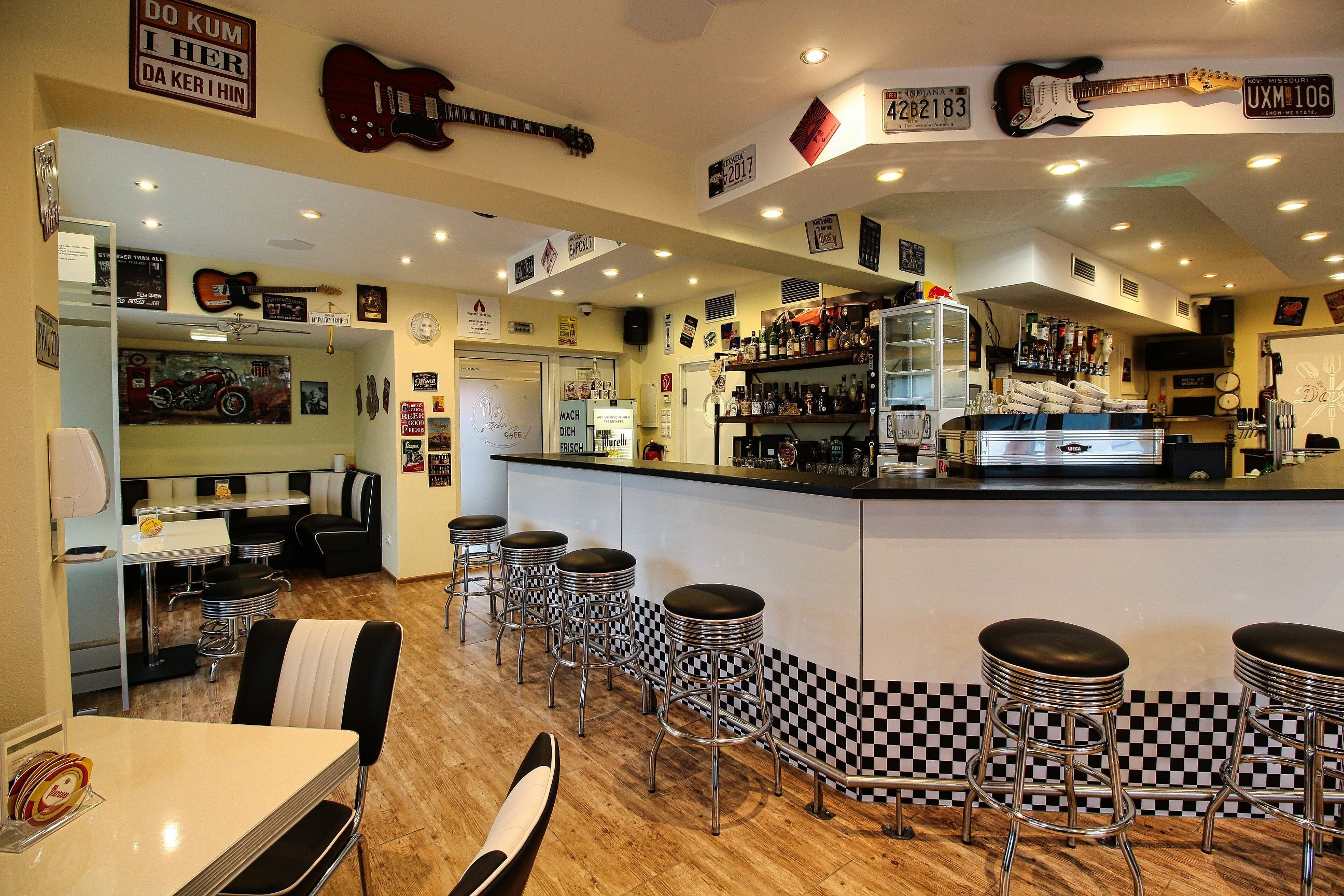 Innenansicht eines Rockabilly-Cafés mit Bar, Hockern und Retro-Dekorationen.