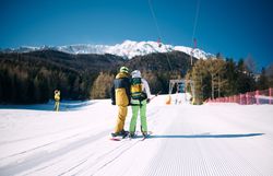 Zwei Skifahrer stehen auf der perfekt präparierten Piste und genießen die atemberaubende Aussicht auf die schneebedeckten Berge. Die klare, kalte Luft und die strahlende Sonne schaffen eine unvergessliche Winteratmosphäre, die zum Verweilen einlädt.