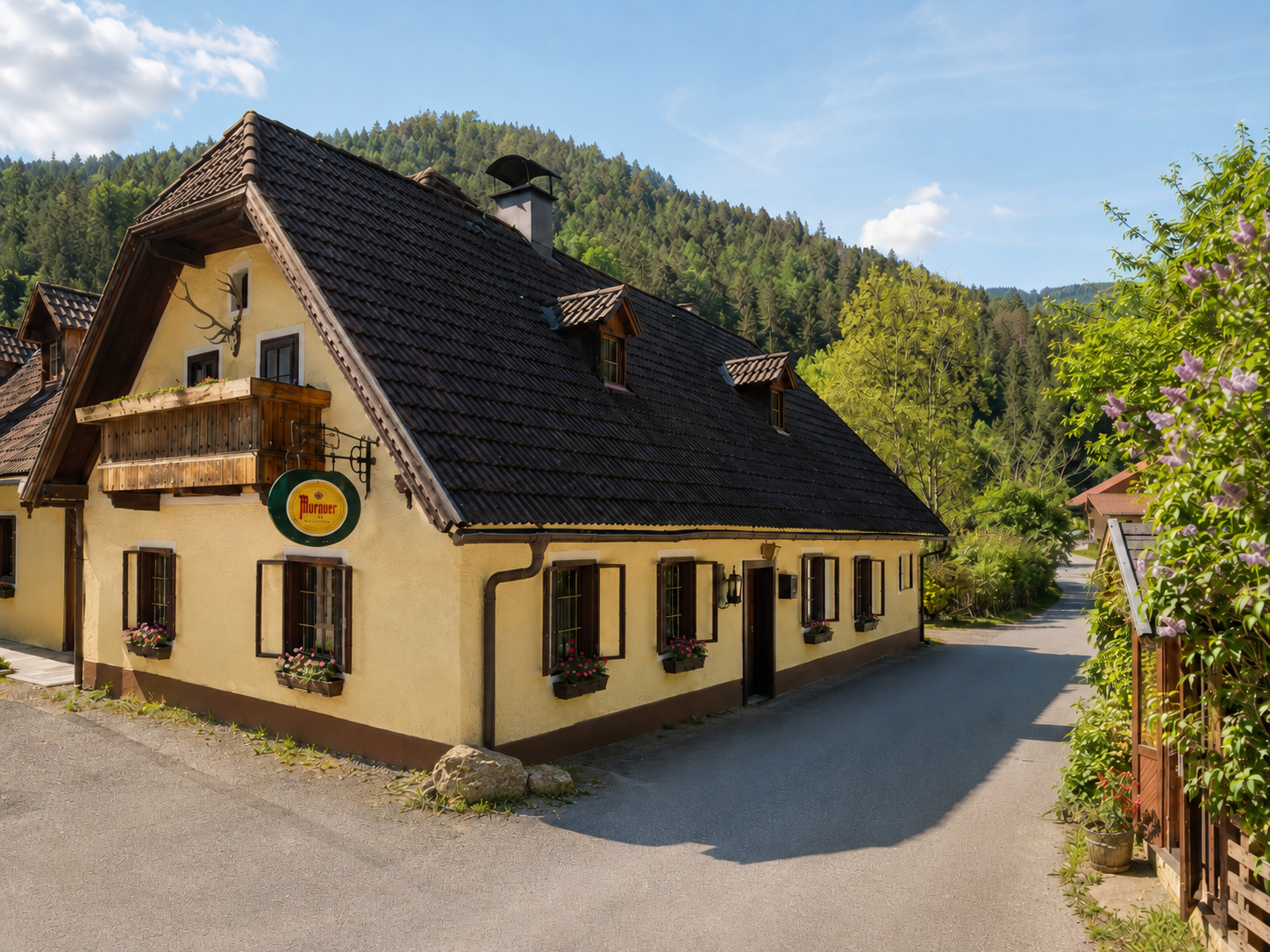 Ein traditionelles Gasthaus mit gelber Fassade und dunklem Schindeldach in einer ländlichen Umgebung mit Wald im Hintergrund.