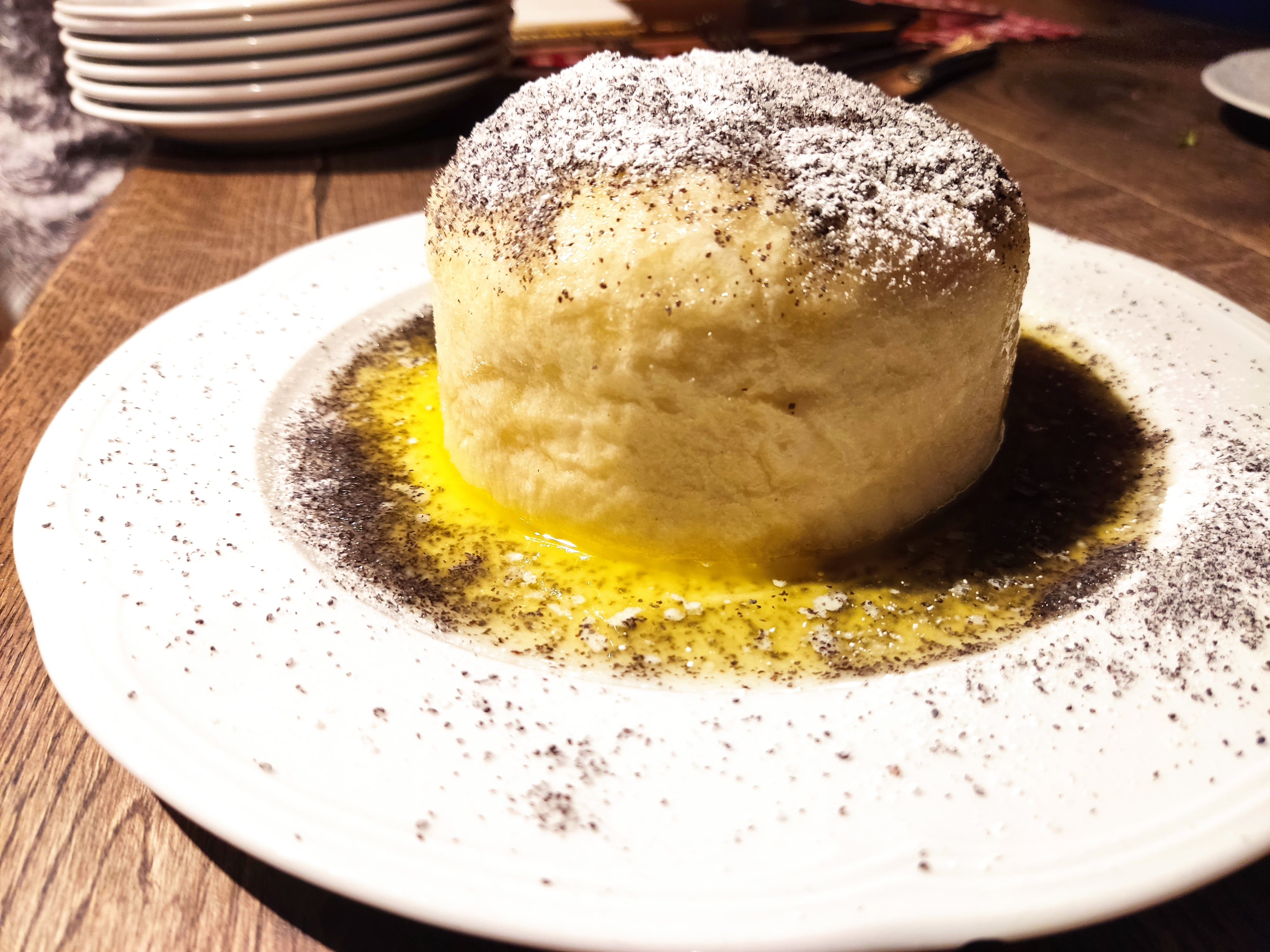 Ein Germknödel mit Mohn und Puderzucker auf einem weißen Teller.