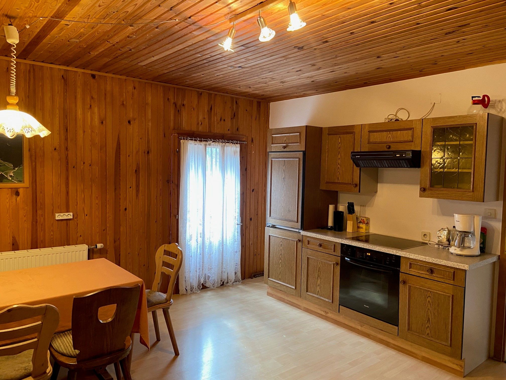 Rustikale Küche mit Holzwänden, Esstisch und Stühlen, sowie moderner Küchenzeile mit Geräten.