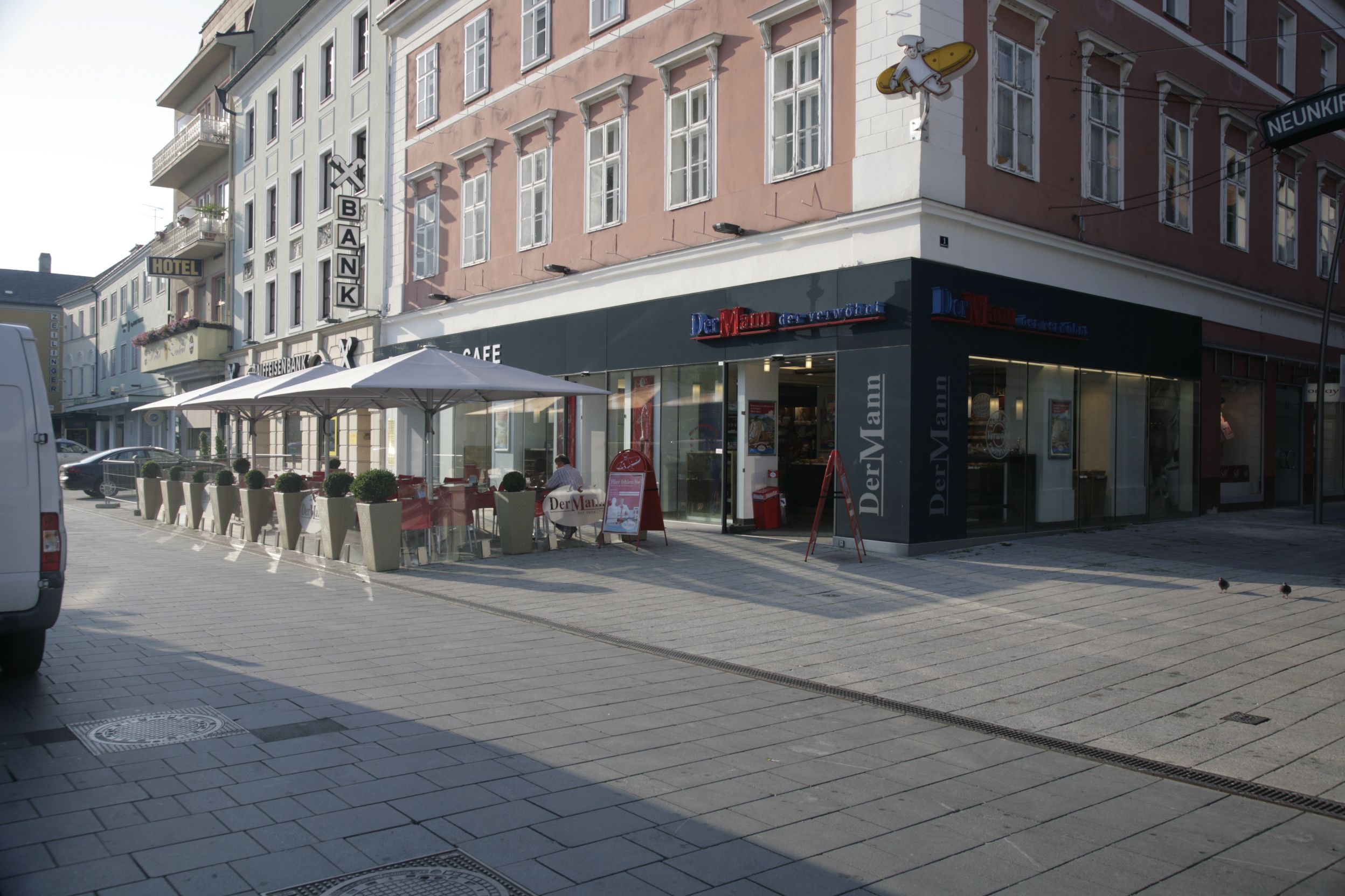 Außenansicht auf Bäckerei DerMann am Hauptplatz. Vor der Bäckerei stehen Tische und Sesseln mit Sonnenschirmen.