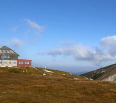 Berghütte steht auf einer Hochebene vor markanter Bergkulisse.