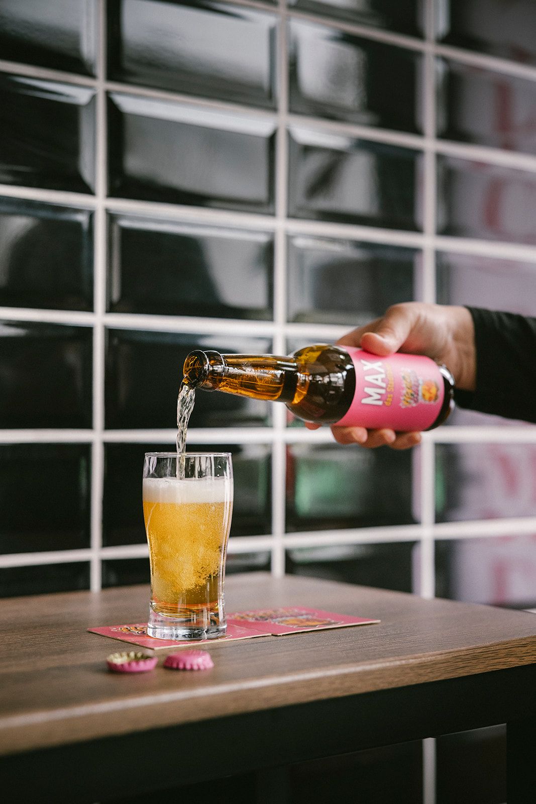 Eine Hand gießt Bier aus einer Flasche mit dem Etikett 'MAX' in ein Glas auf einem Tisch.