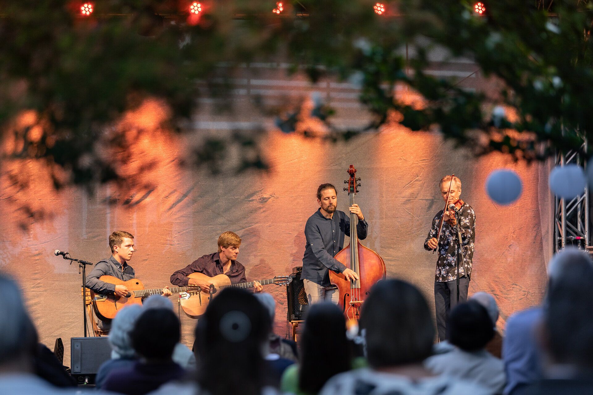 Auf einer Bühne geben vier Musiker ein Open Air Konzert vor Publikum.