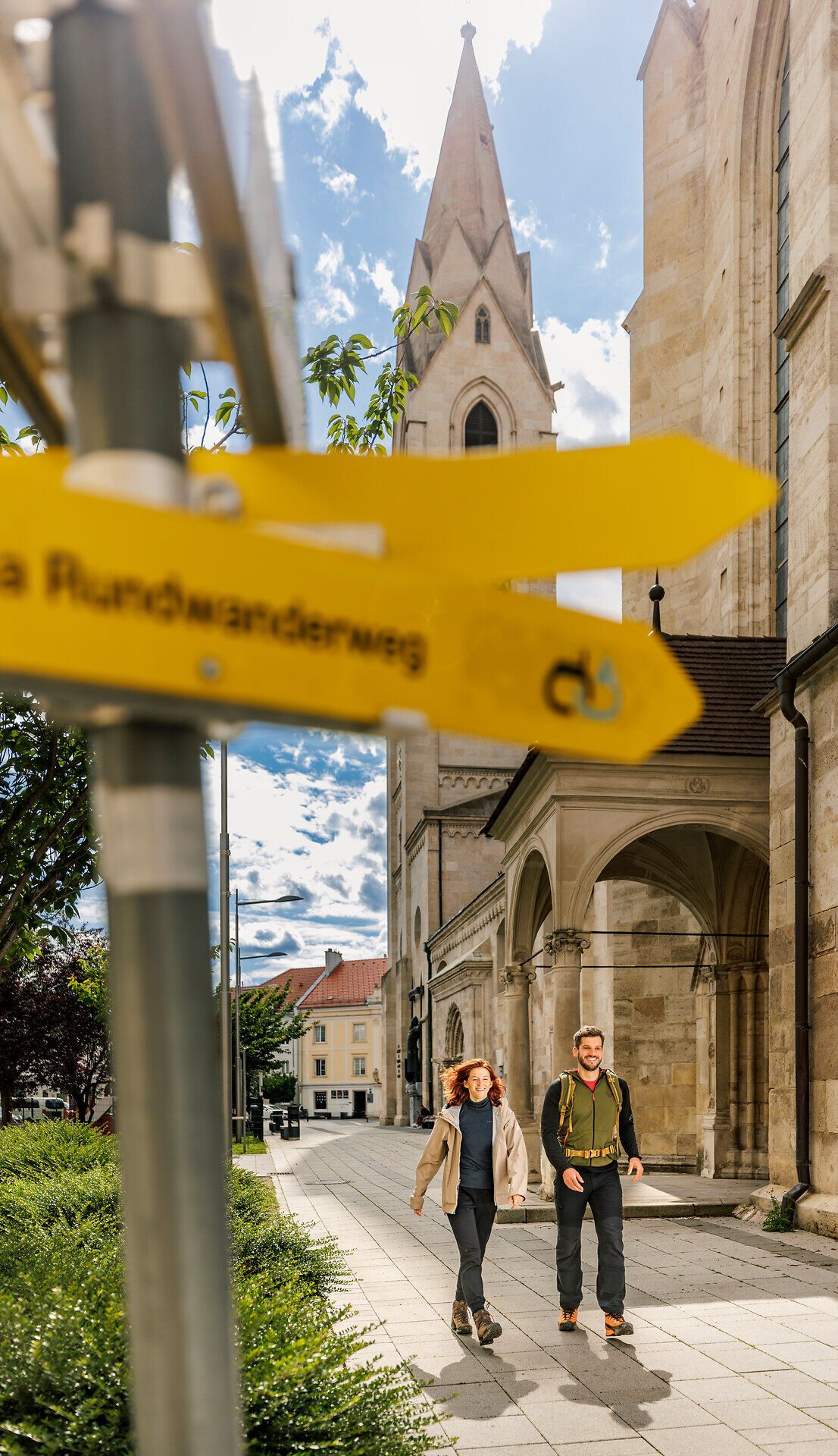 Ein Frau und ein Mann spazieren neben dem Wiener Neustädter Dom entlang.