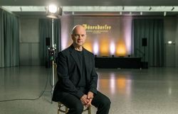 Florian Krumböck, Intendant des Bösendorfer Festivals in Wiener Neustadt, sitzt in schwarzer Kleidung auf einem Sessel vor einer beleuchteten Veranstaltungsbühne.