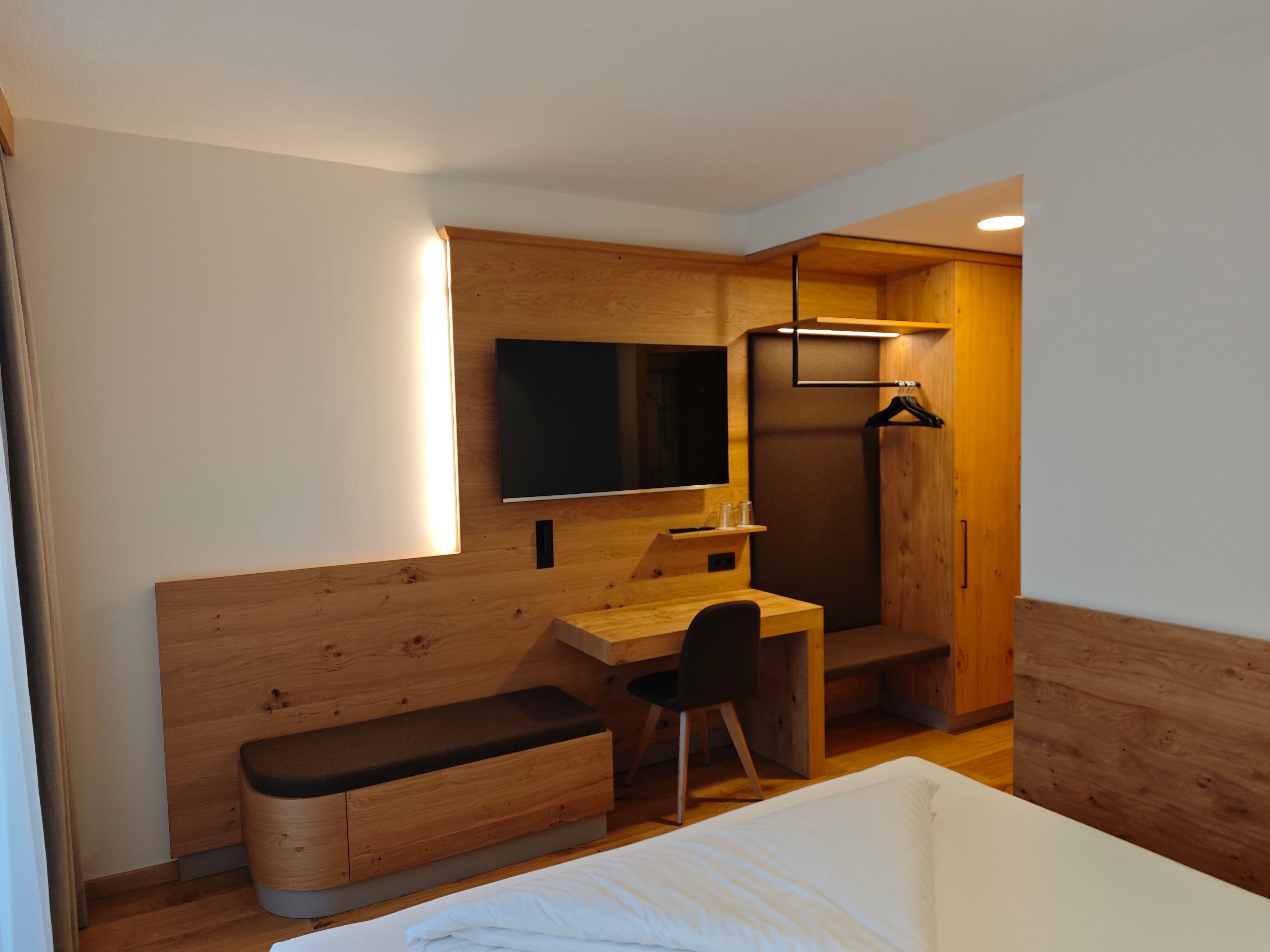 Modern eingerichtetes Hotelzimmer mit Holzmöbeln, einem Schreibtisch, einem Fernseher und einem Kleiderschrank.