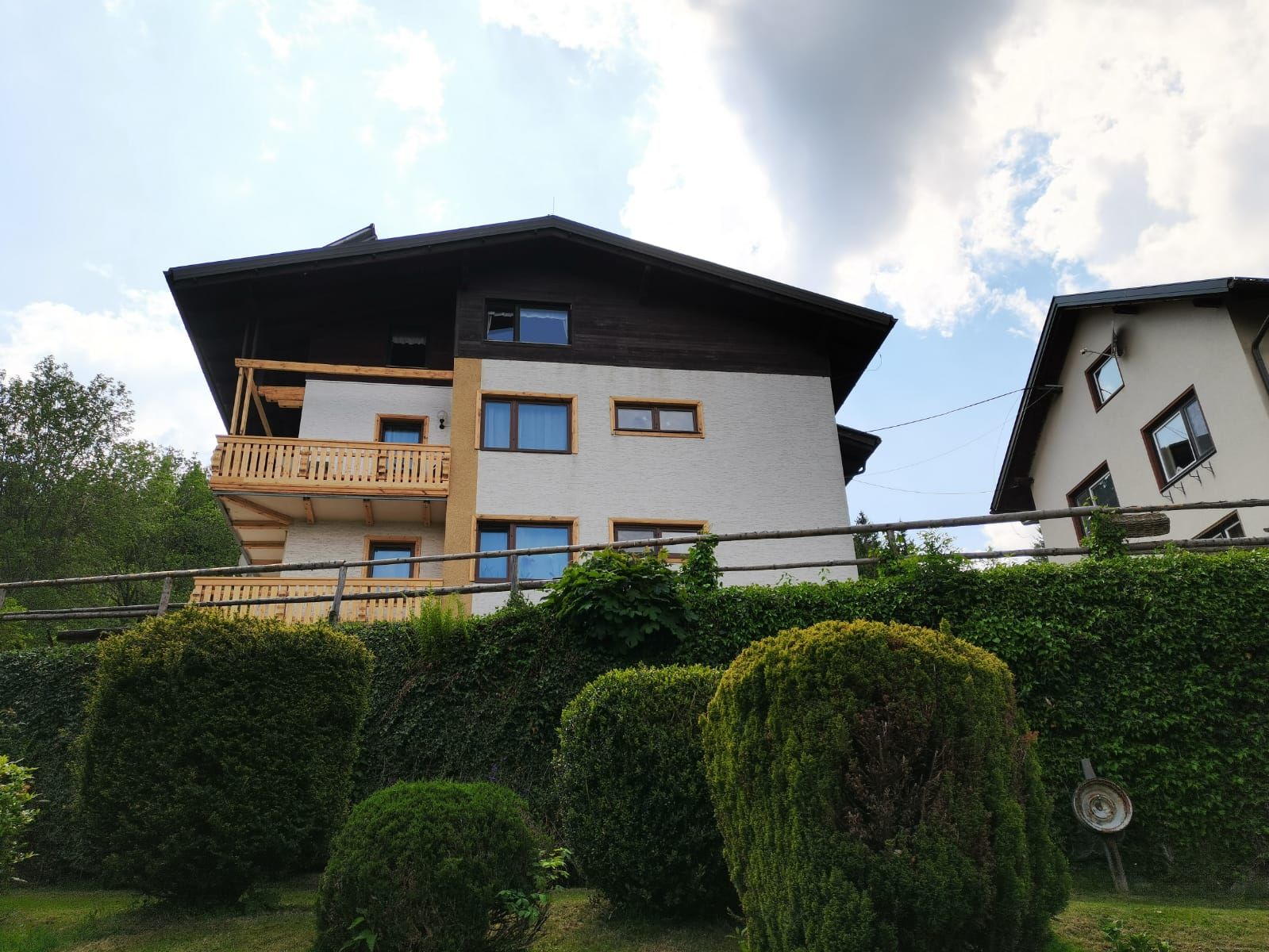 Zweistöckiges Haus mit Holzbalkon und Garten im Vordergrund.
