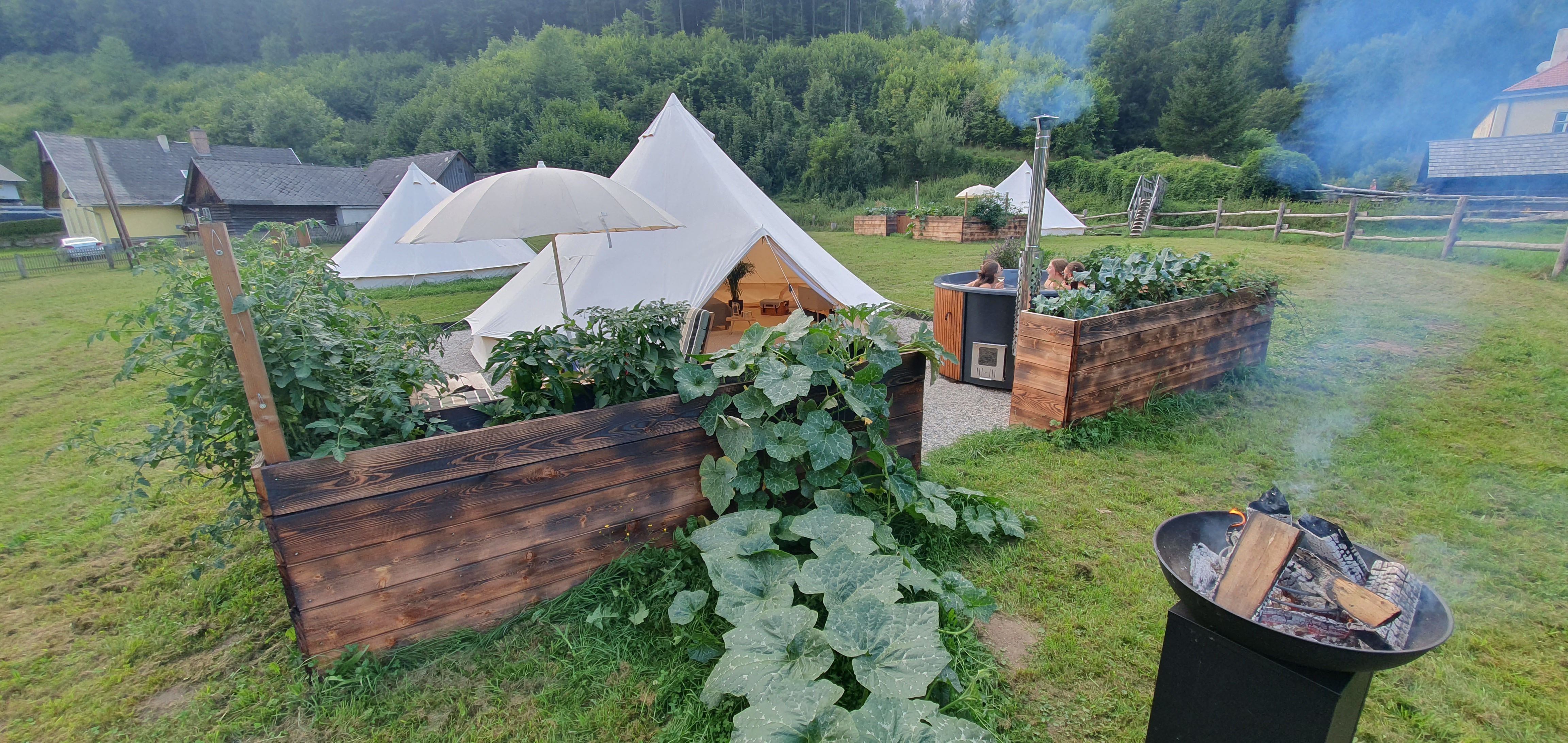 Glamping-Zeltplatz mit Feuerstelle und Hot Tub in grüner Umgebung.