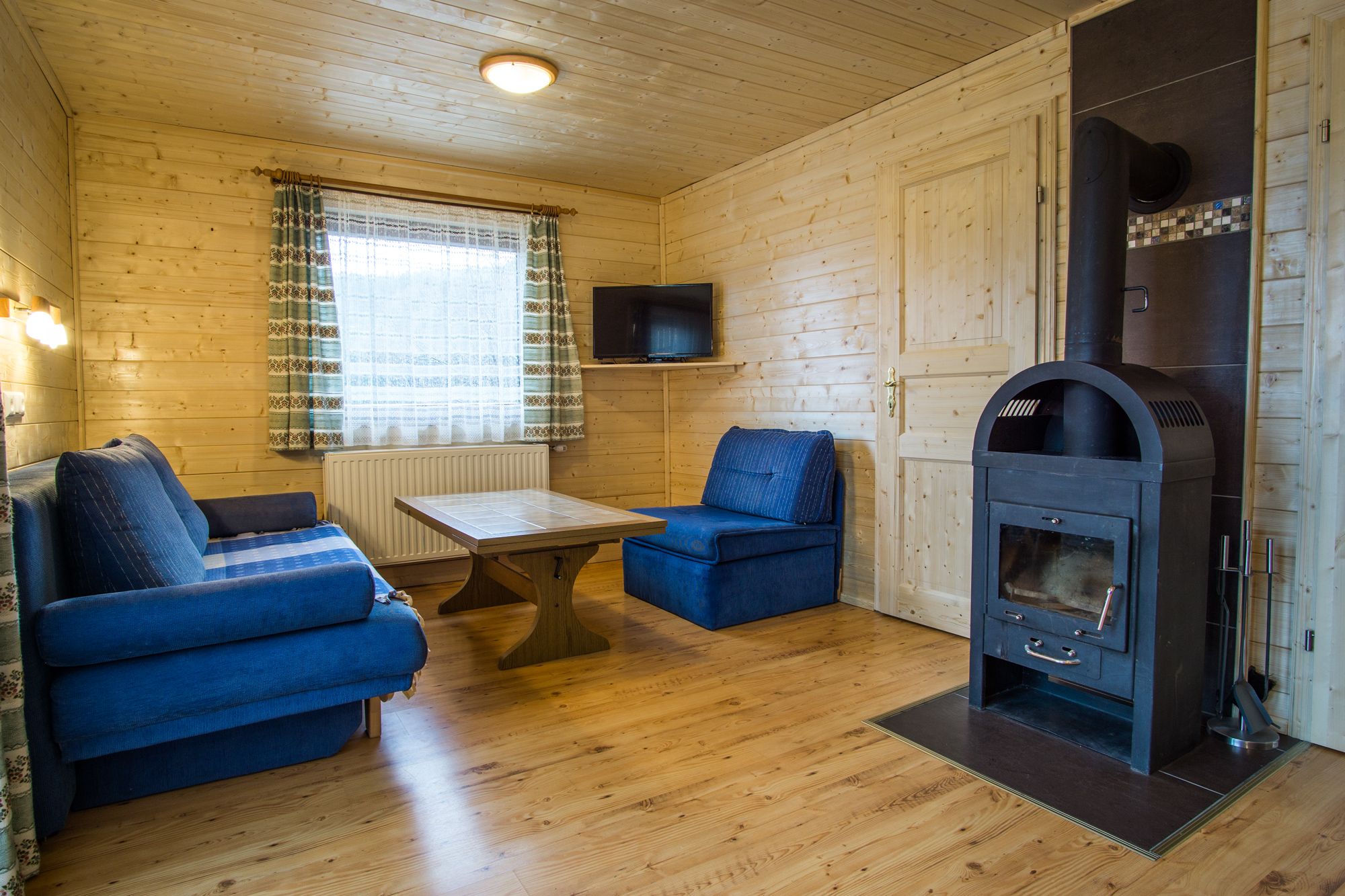 Gemütliches Wohnzimmer mit Holzwänden, blauen Sofas, Holztisch und Kaminofen.