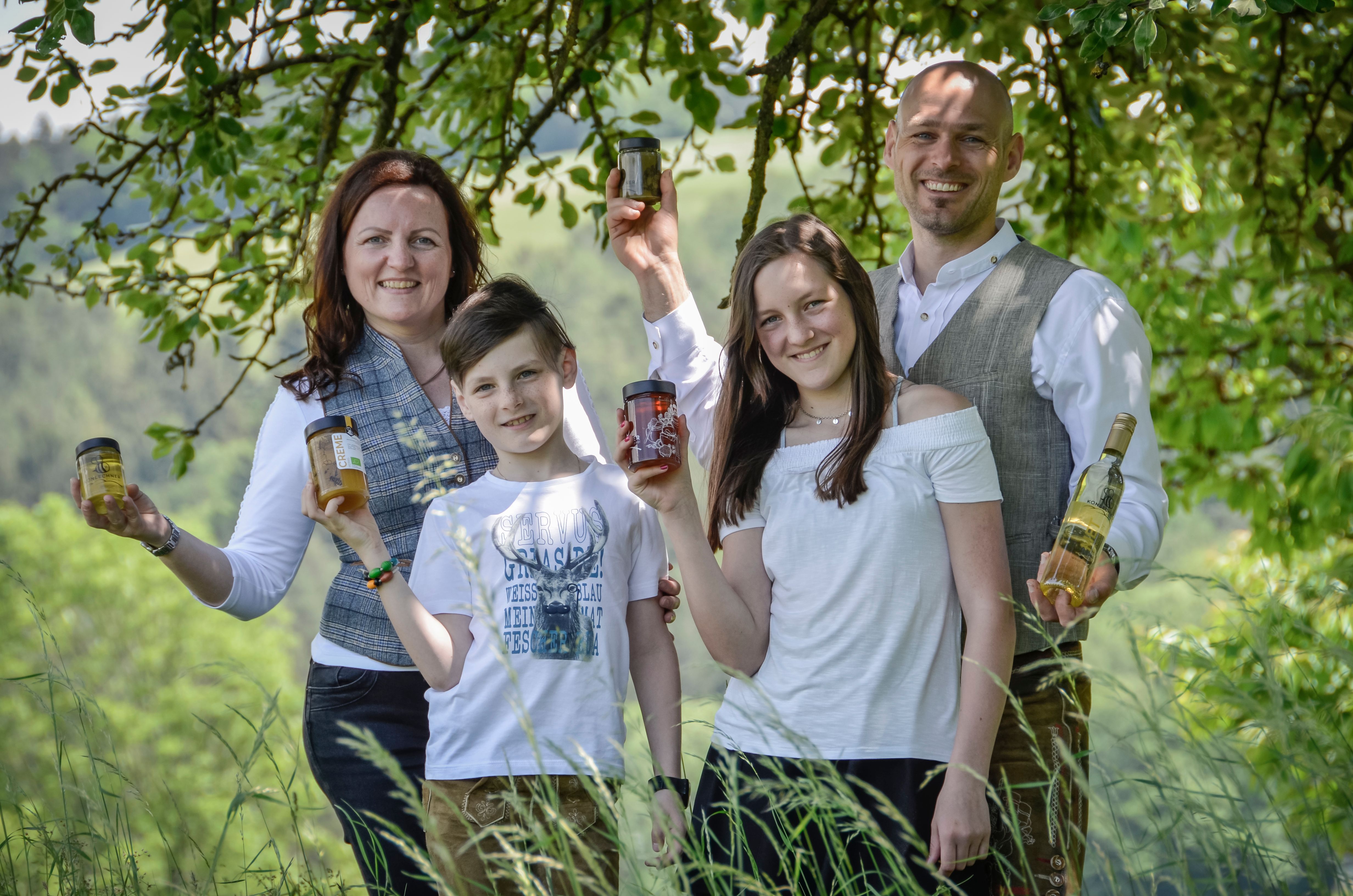 Eine Familie mit zwei Kindern steht auf einer Wiese und hält verschiedene Honigprodukte.