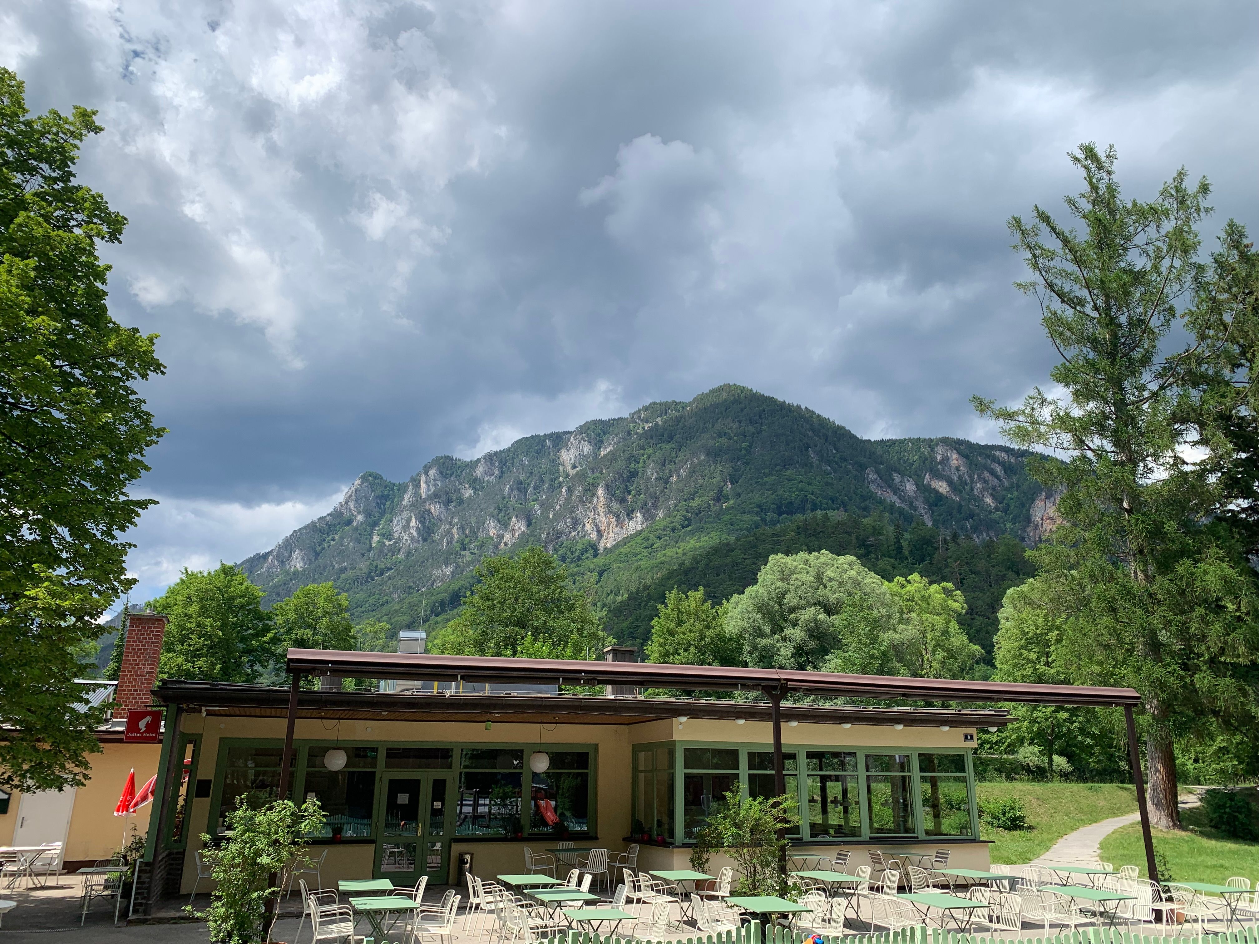 Ein Café mit Terrasse vor einer Bergkulisse und bewölktem Himmel.