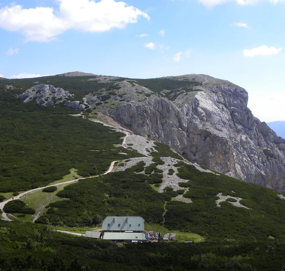 Berglandschaft auf der Rax mit markanten Felsformationen, Wanderwegen und einer Schutzhütte unter blauem Himmel.