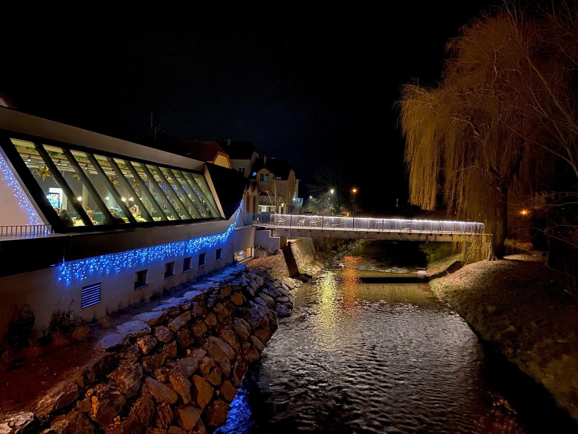 Nachtszene mit beleuchtetem, modernen Gebäude und Fluss.