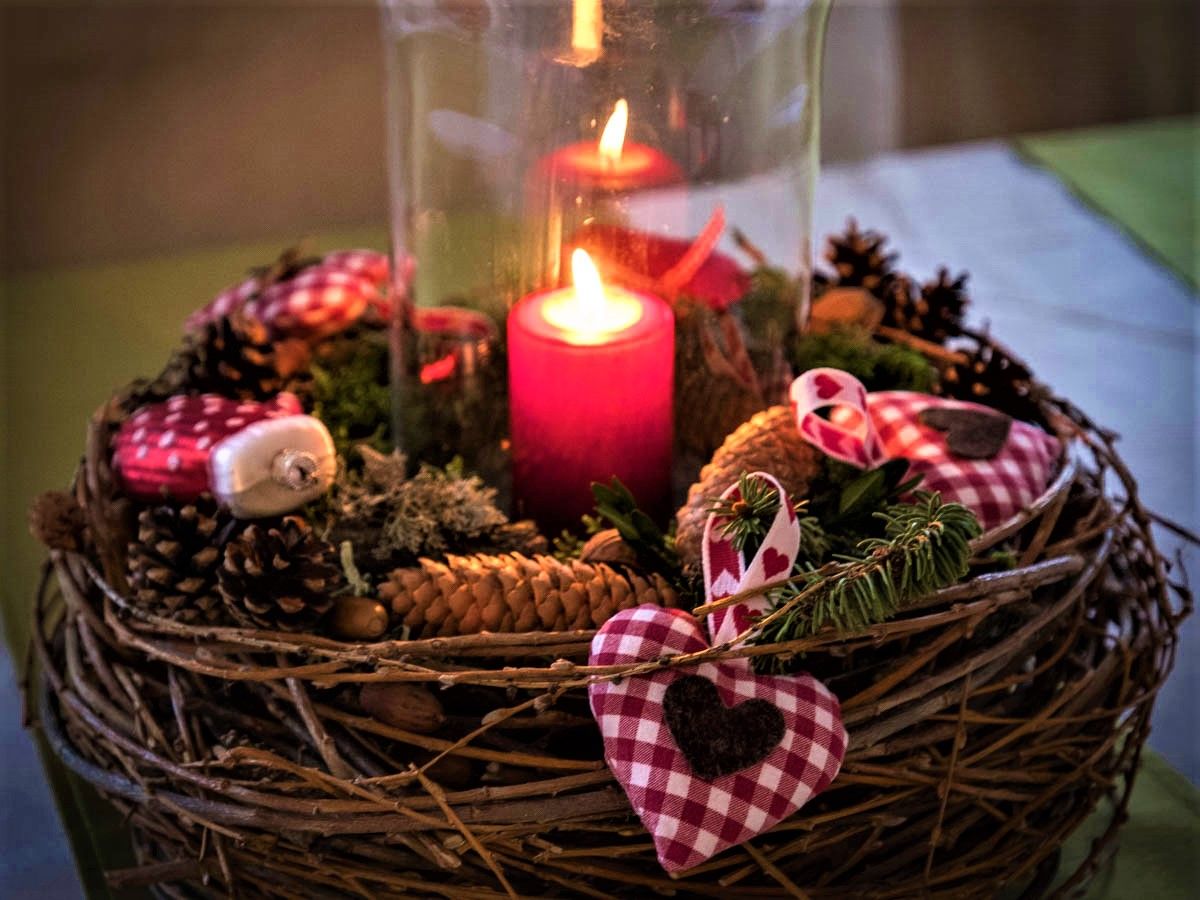 Ein Adventskranz mit einer brennenden roten Kerze, Tannenzapfen und rot-weiß karierten Stoffherzen.