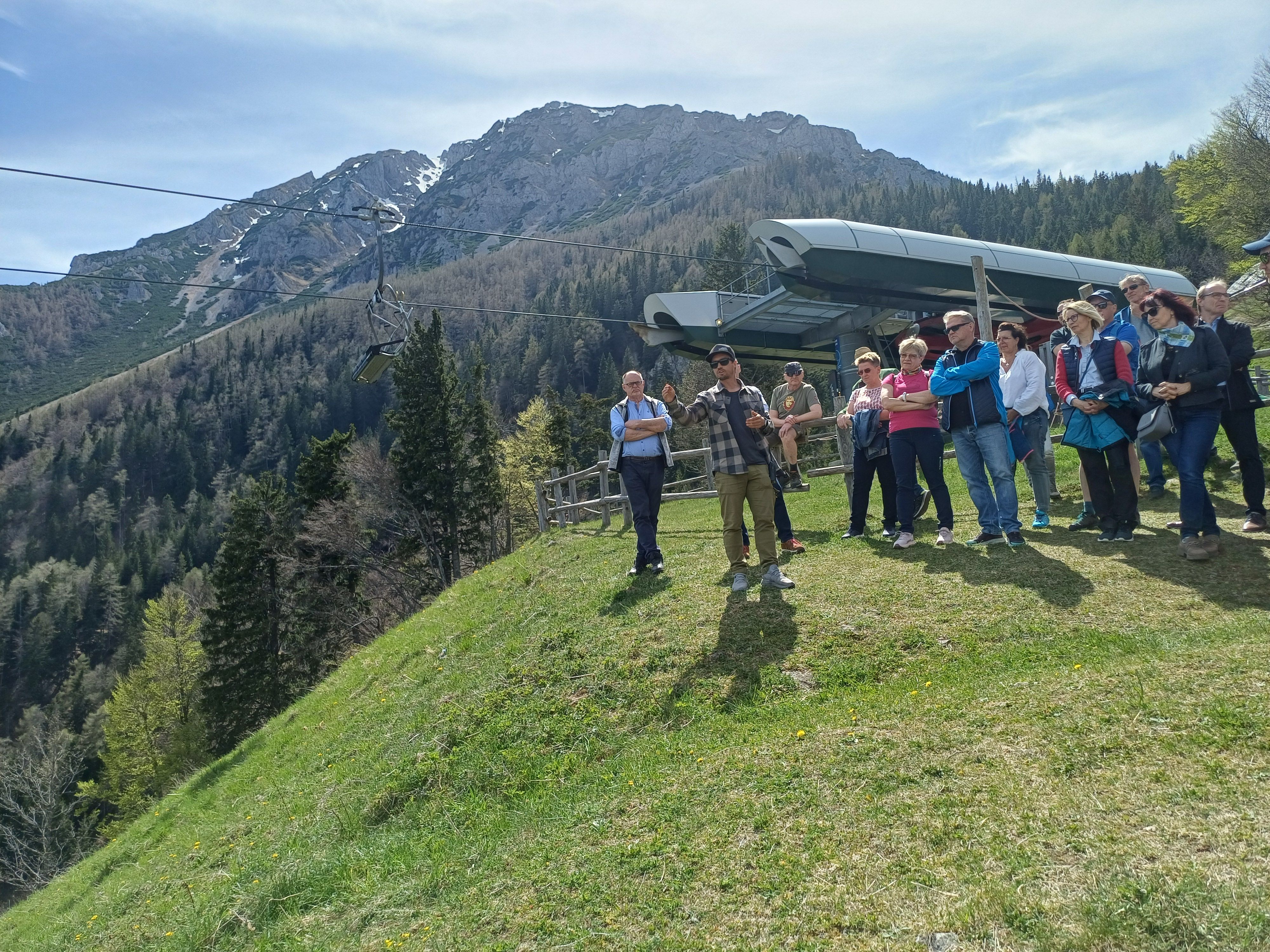 Eine Gruppe von rund 15 Personen steht vor einer Sessellift Bergstation und blickt in die Ferne.