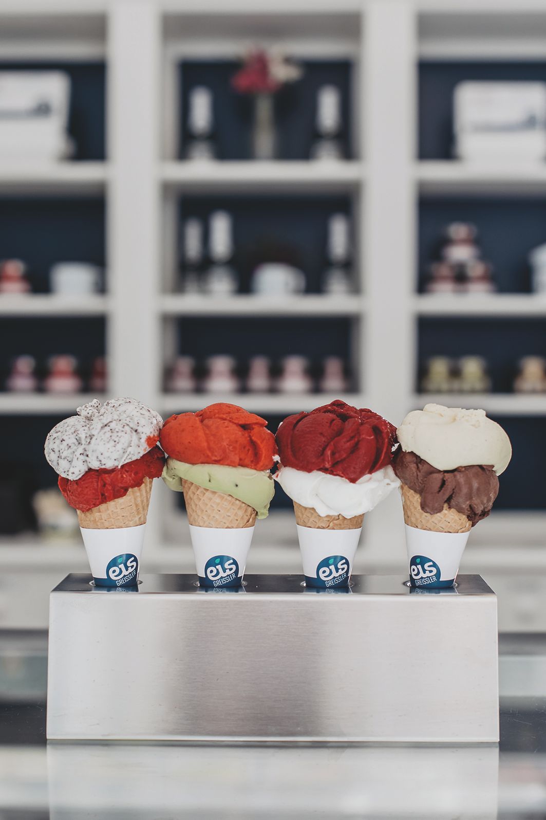 Metallhalterung mit vier Eiswaffeln, jeweils mit zwei Kugeln unterschiedlicher Eissorten.