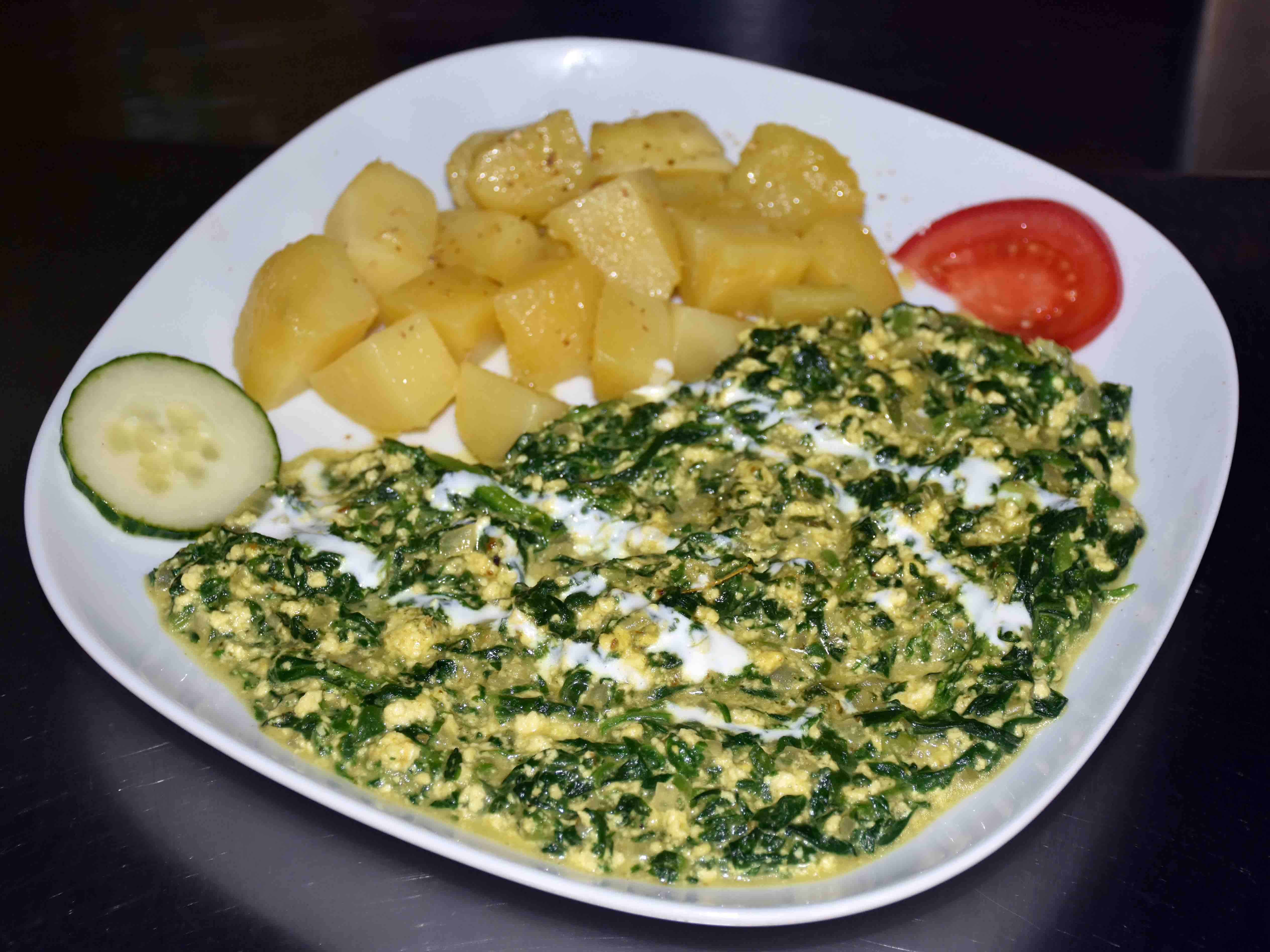 Ein Teller mit einem indischen Gemüsegericht mit Kartoffeln, garniert mit einem Stück Tomate und Gurke.