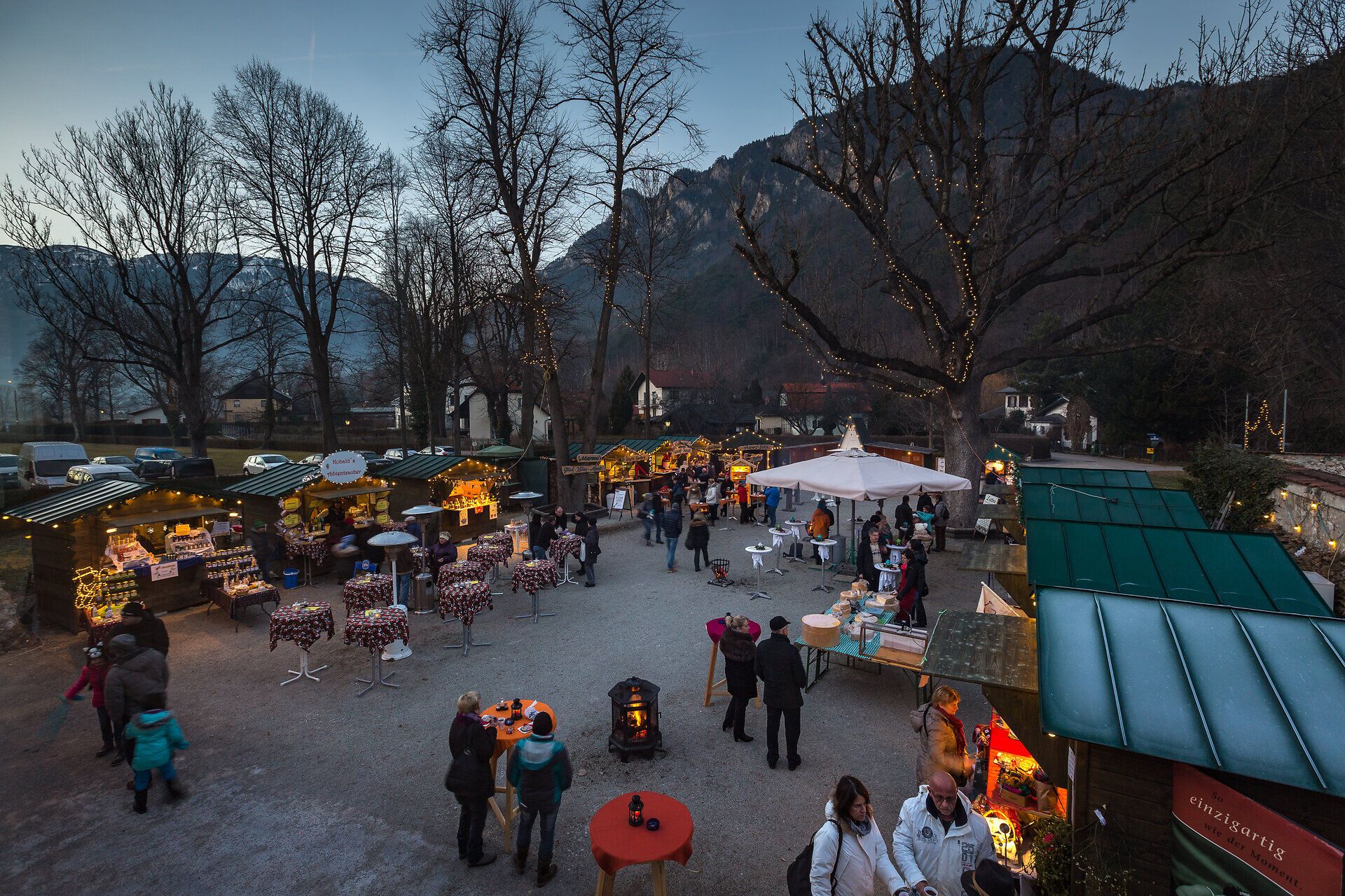 Adventmarkt im Schloss Reichenau an der Rax. Das Schloss ist von außen stimmungsvoll beleuchtet, im Innenhof stehen die Hütten. Menschen stehen davor und trinken Punsch.