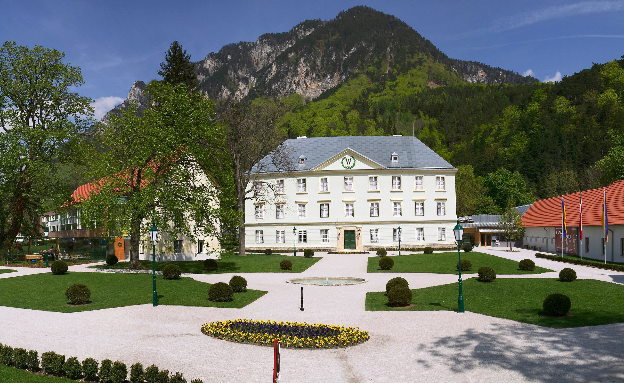 Schloss Reichenau vor einer Bergkulisse mit gepflegtem Garten im Vordergrund.