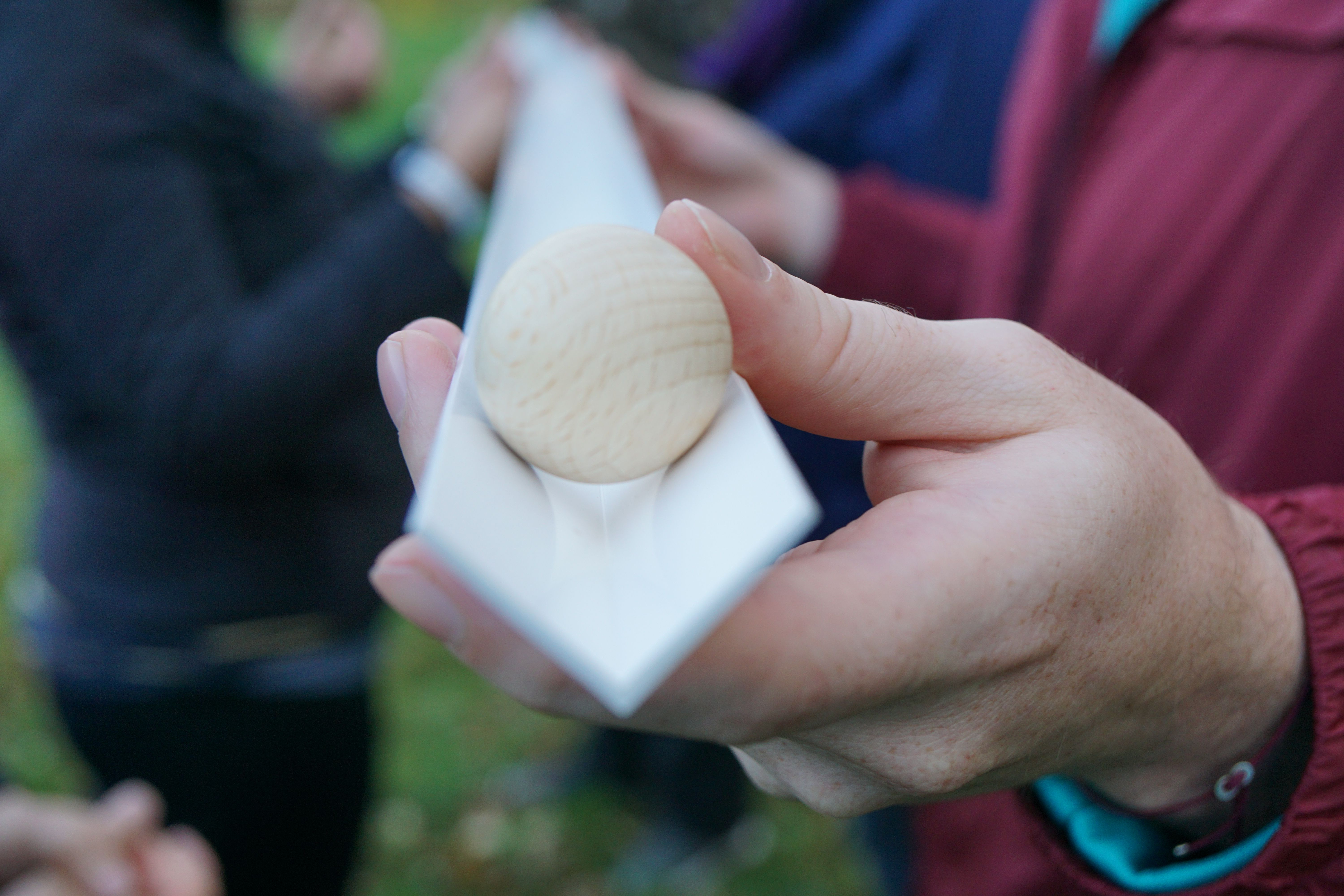 Nahaufnahme einer Hand, die eine weiße Rinne mit einer Holzkugel darin hält.