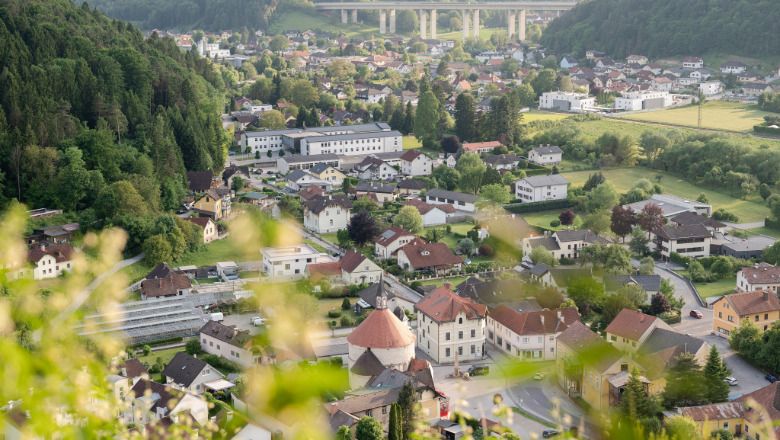 Blick auf Scheiblingkirchen mit Rundkirche und umliegenden Häusern, im Hintergrund eine Autobahnbrücke und bewaldete Hügel.