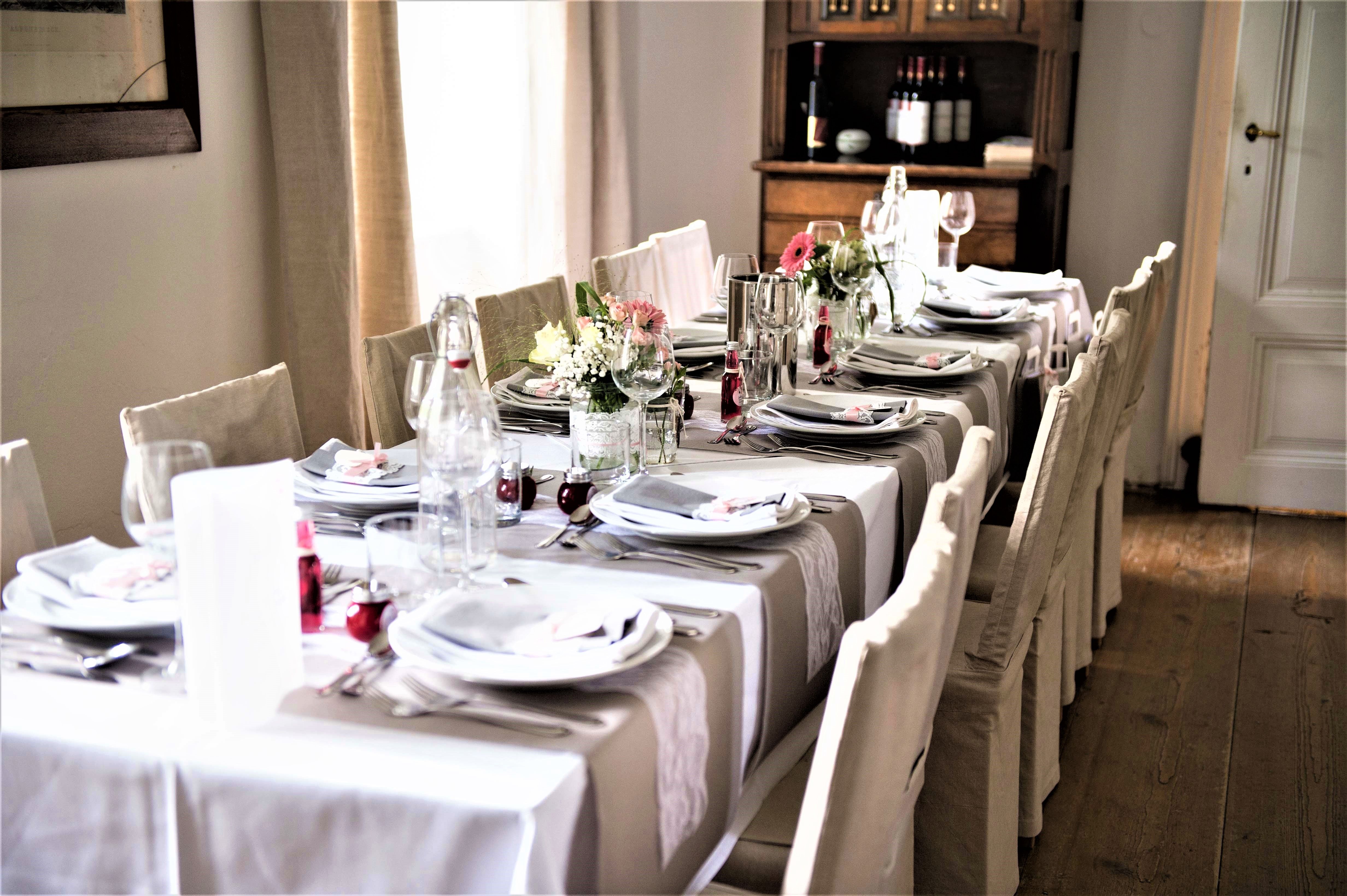 Elegant gedeckter Tisch mit weißen Tischdecken, Blumenarrangements und Geschirr in einem Raum mit Holzboden.